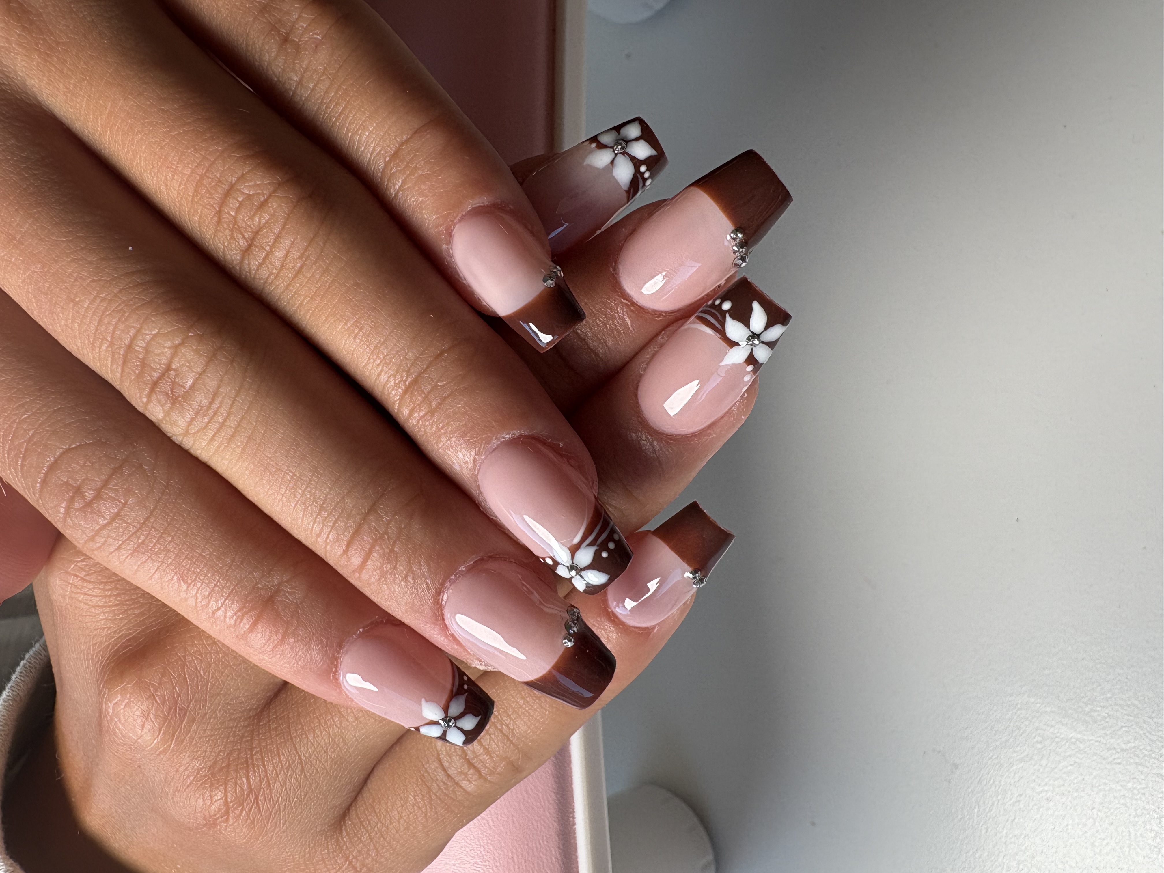 Nude square nails with brown French tips, white flower accents, and rhinestones