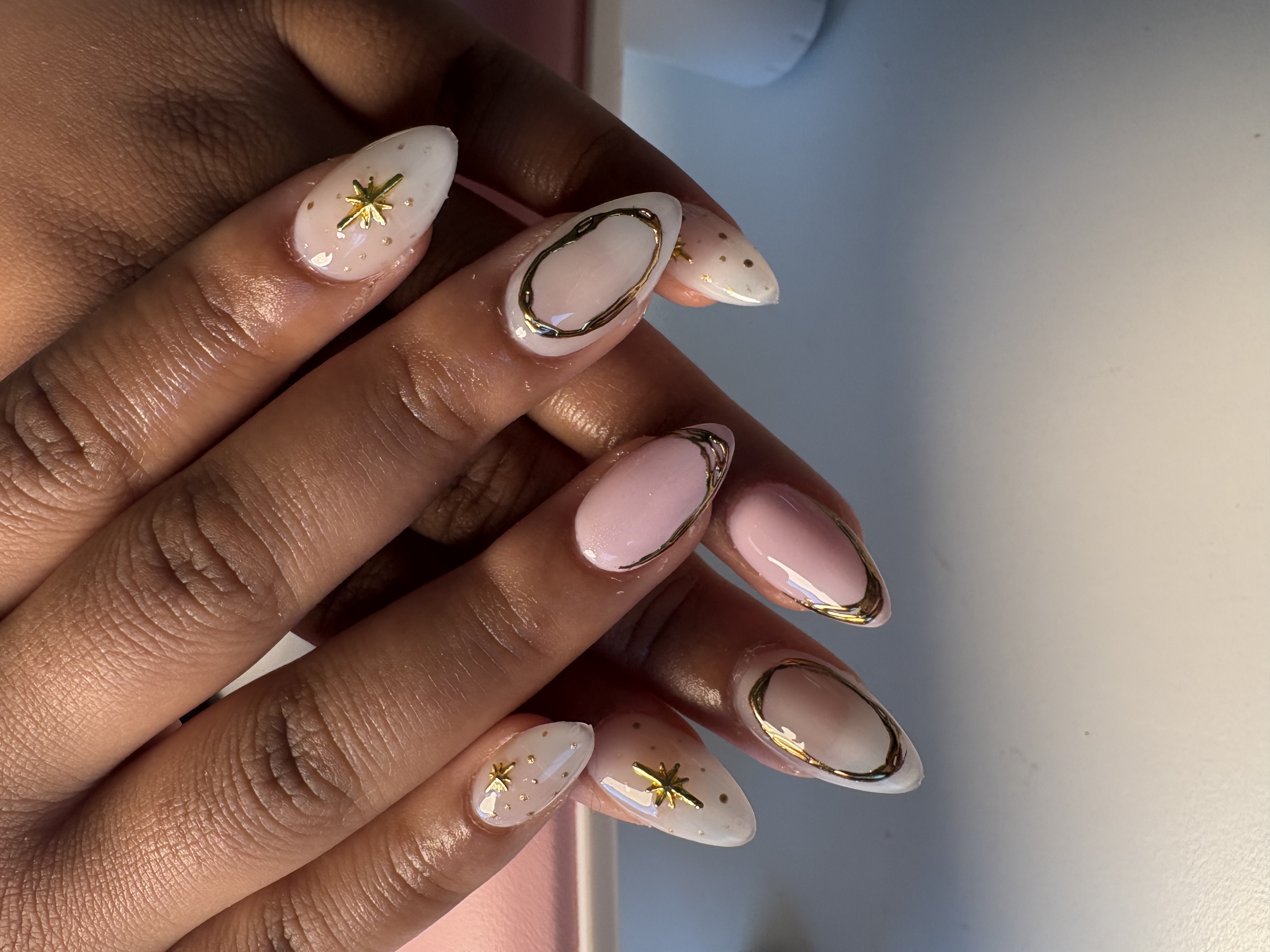 Nude almond nails with gold chrome linework loops and gold star charm accents