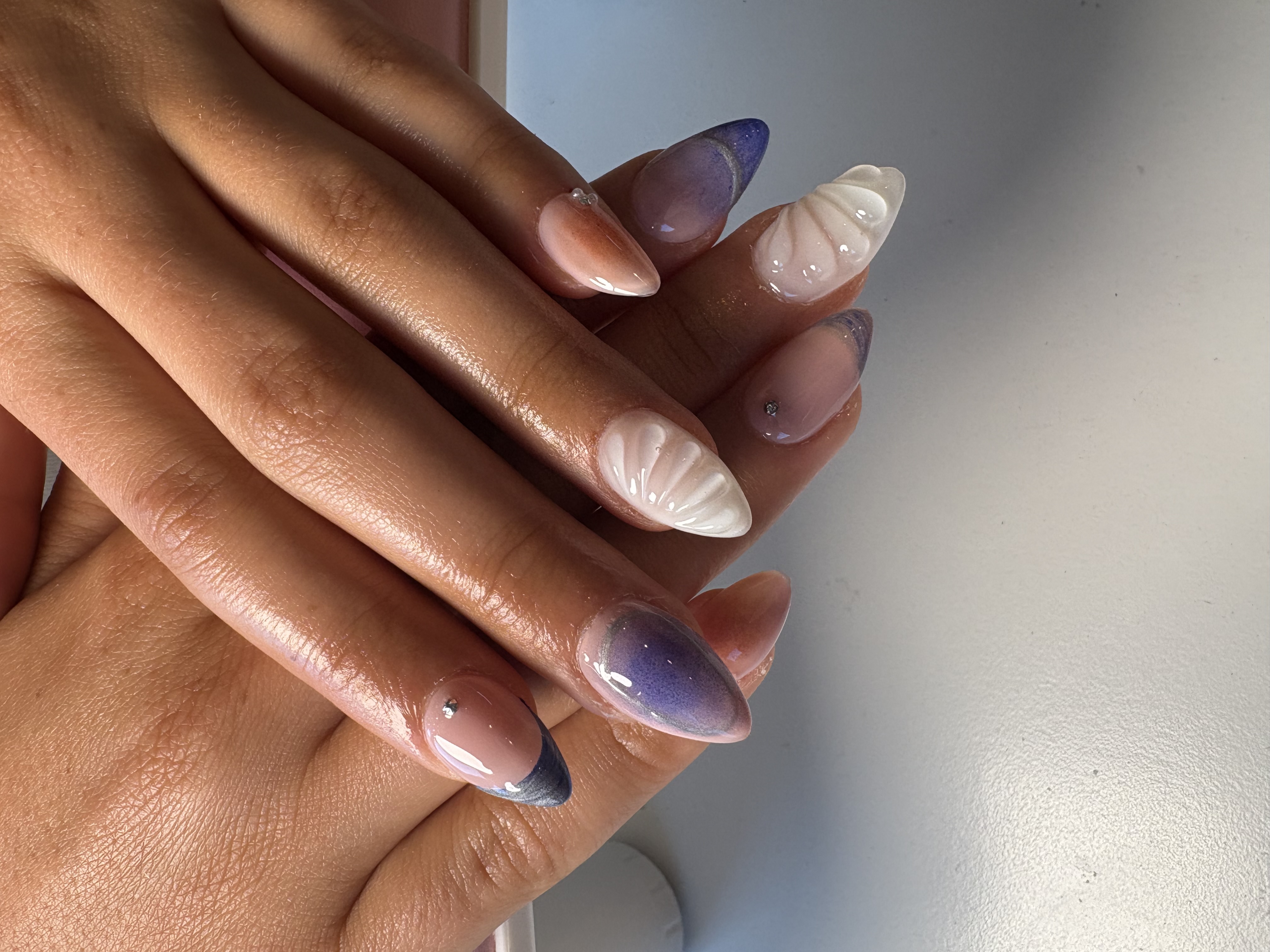 Nude almond nails with purple ombre tips and 3D carved white shell accents
