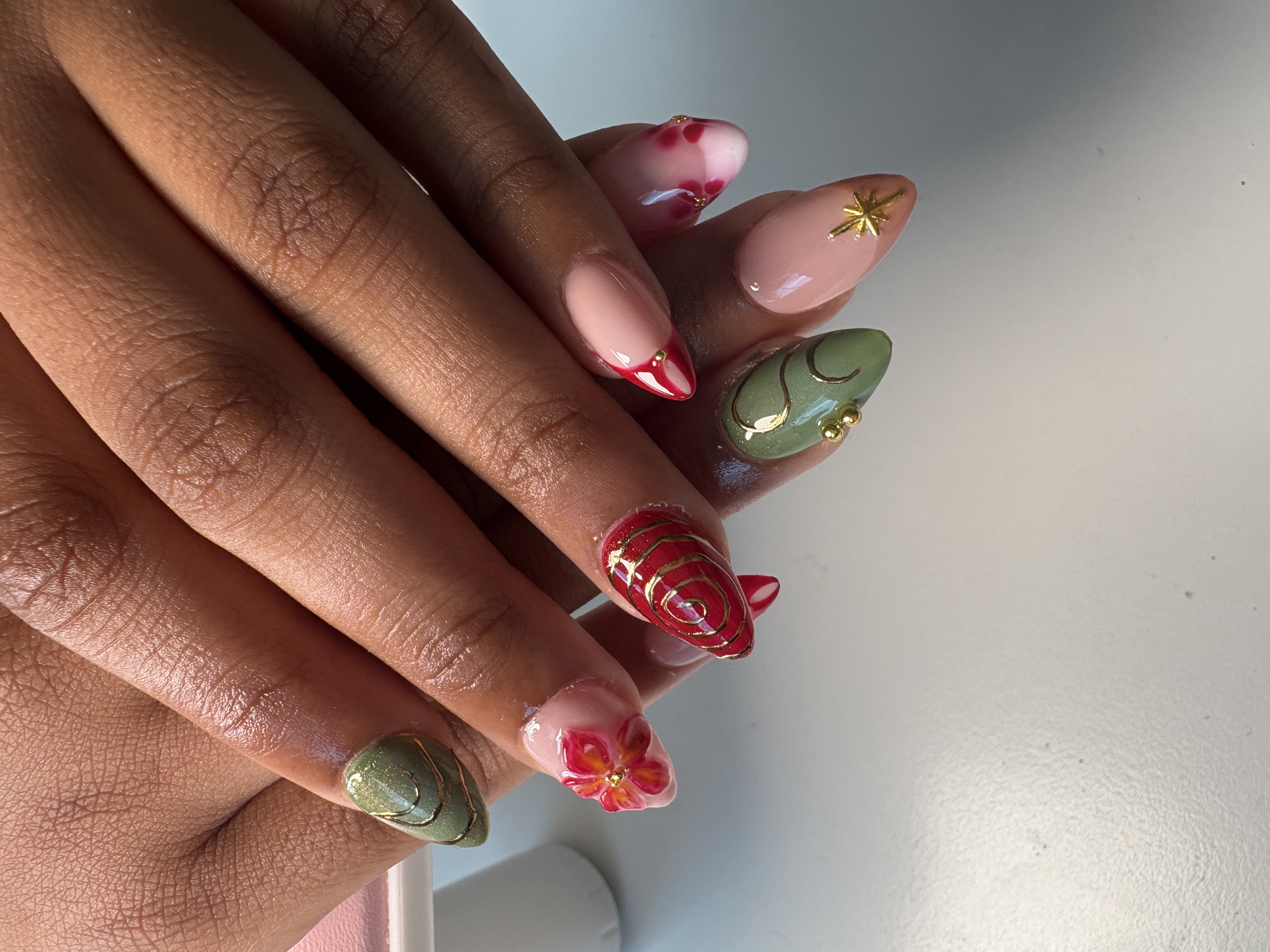 Mixed pink, red, and green almond nails with gold spiral linework and painted flowers