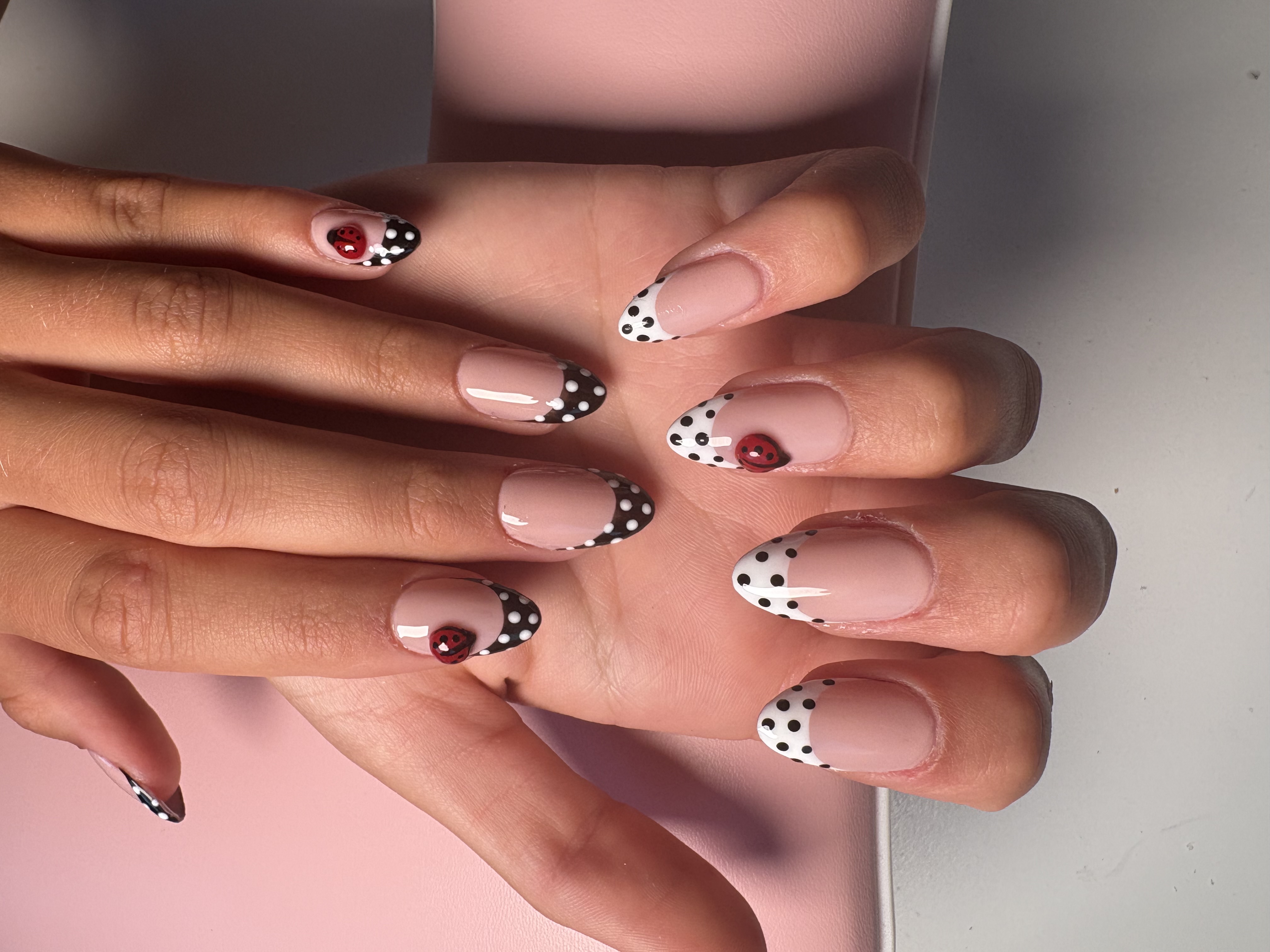 Nude nails with black-and-white polka dot French tips and 3D ladybug accents