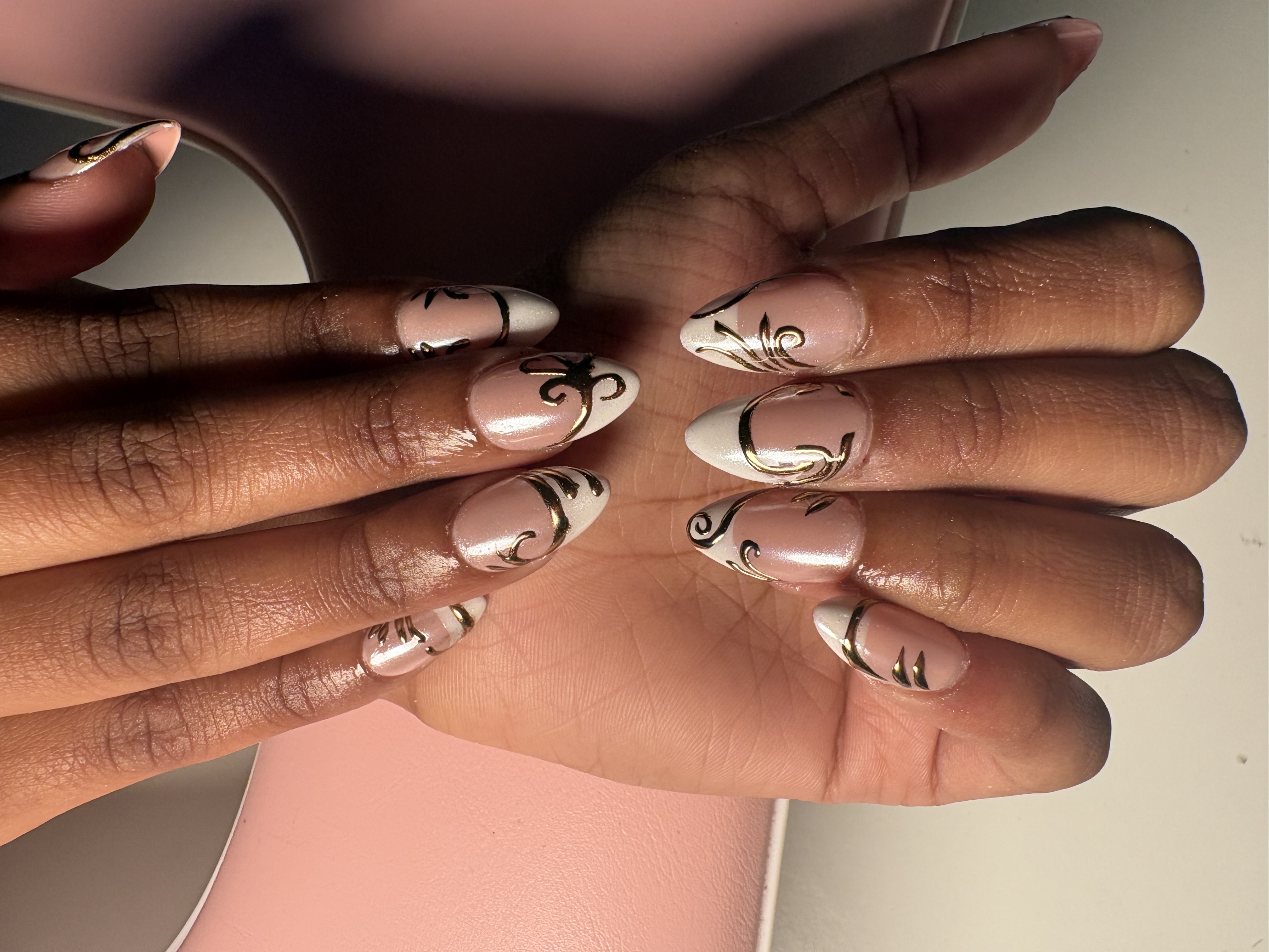 Nude French tip almond nails with intricate gold scroll and vine linework