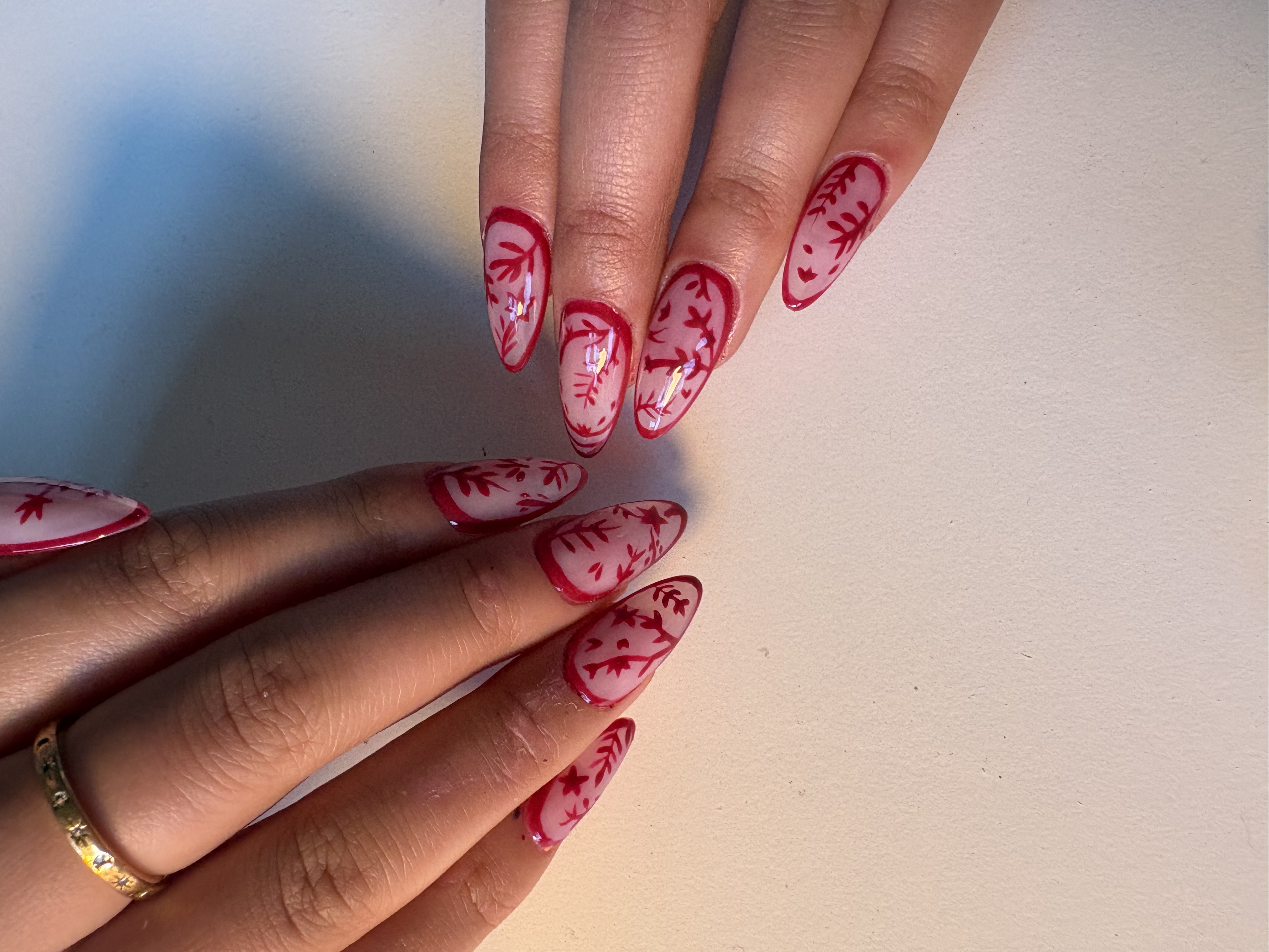 Nude almond nails with fine red hand-painted branch and leaf linework