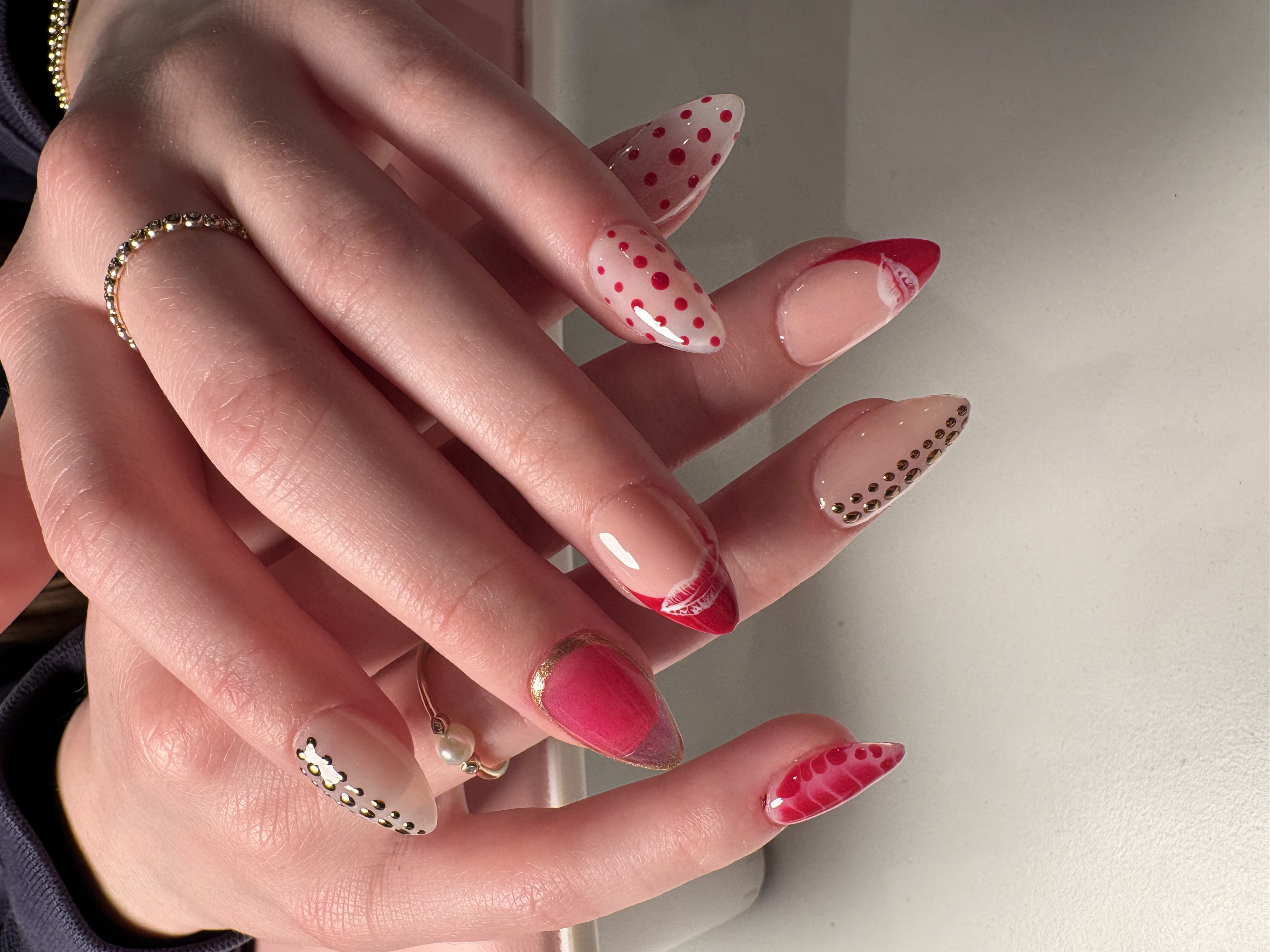 Nude stiletto nails with red polka dot tips, lip art, and gold stud accents