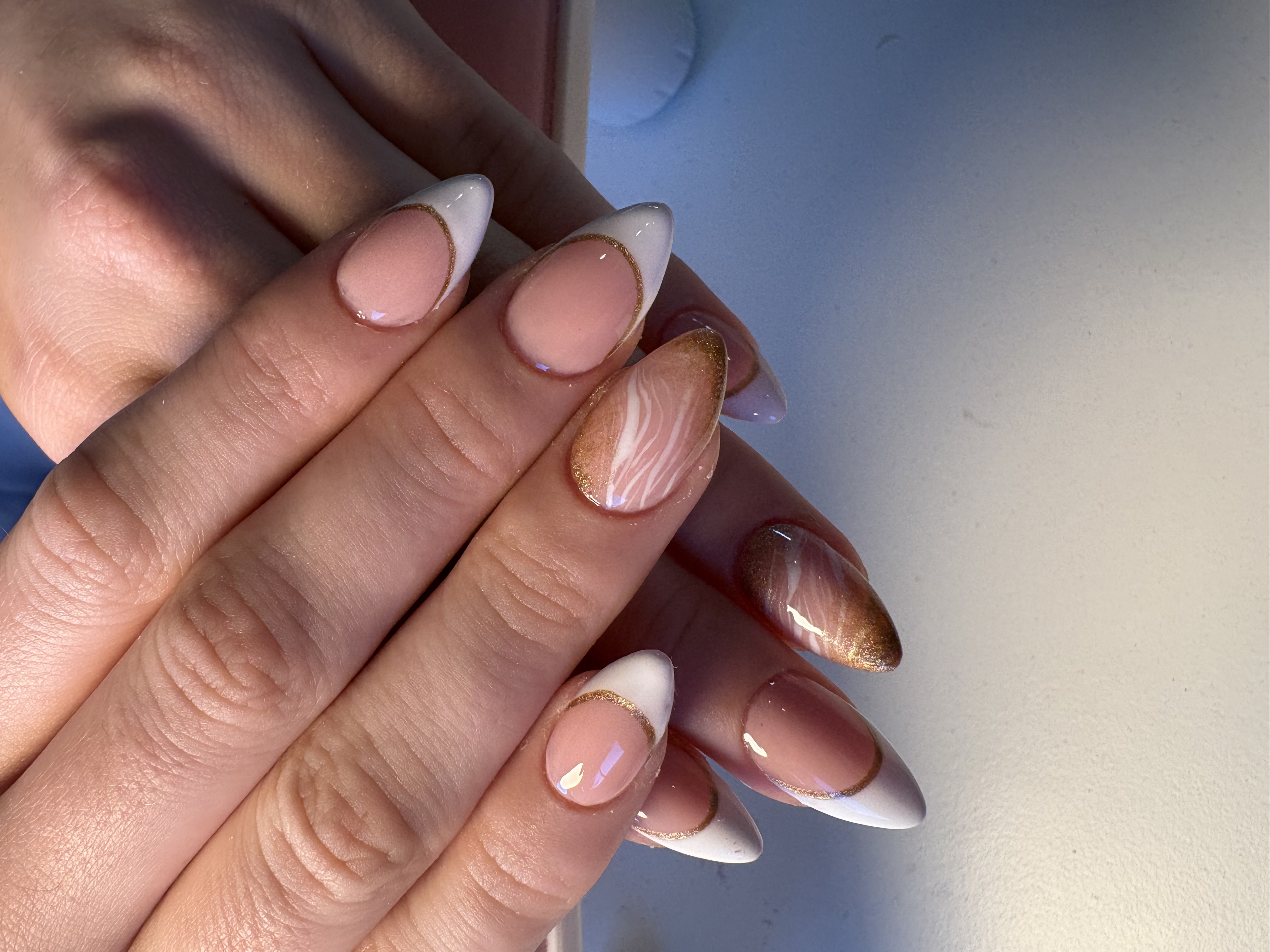 Nude almond nails with gold-outlined white French tips and a marbled gold accent nail