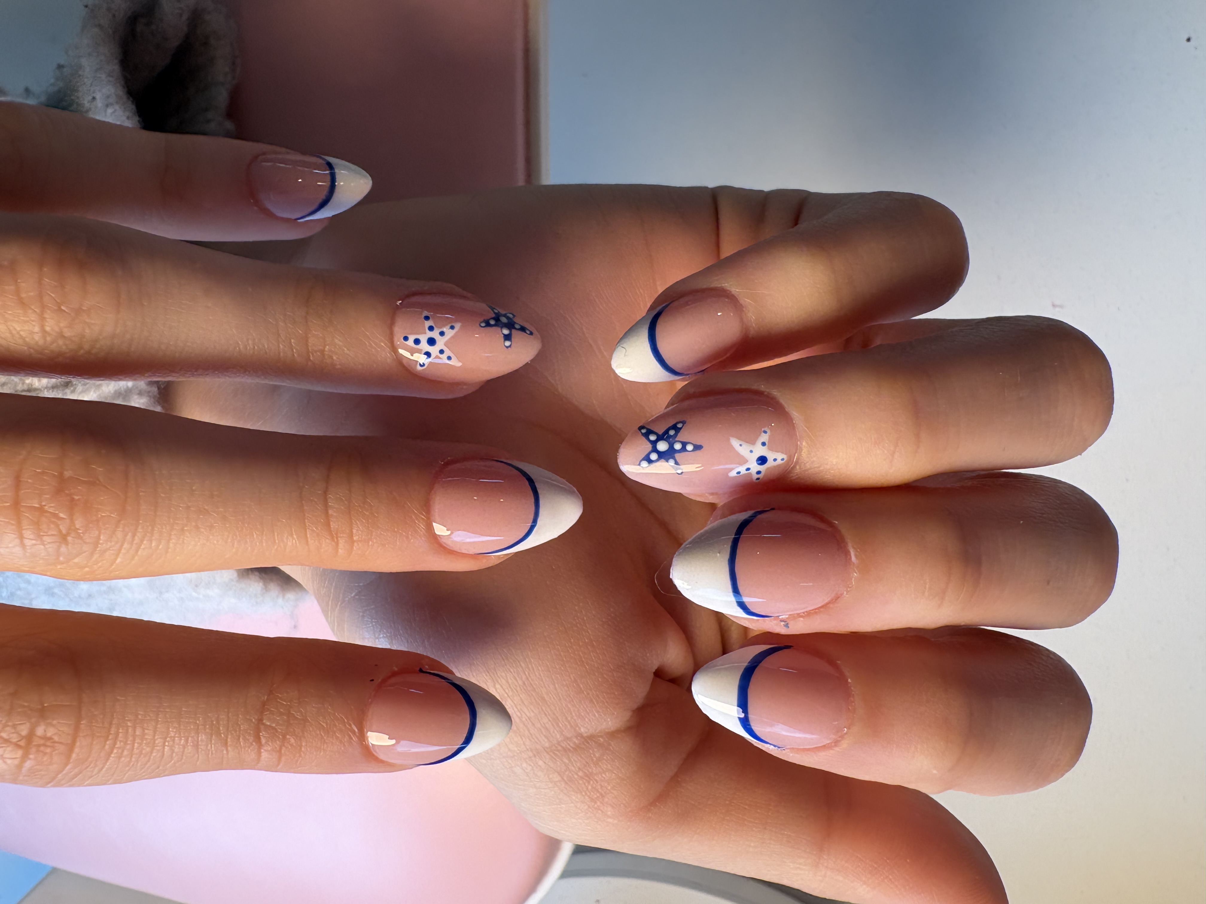 Nude almond nails with navy French tips and two hand-painted starfish accent nails