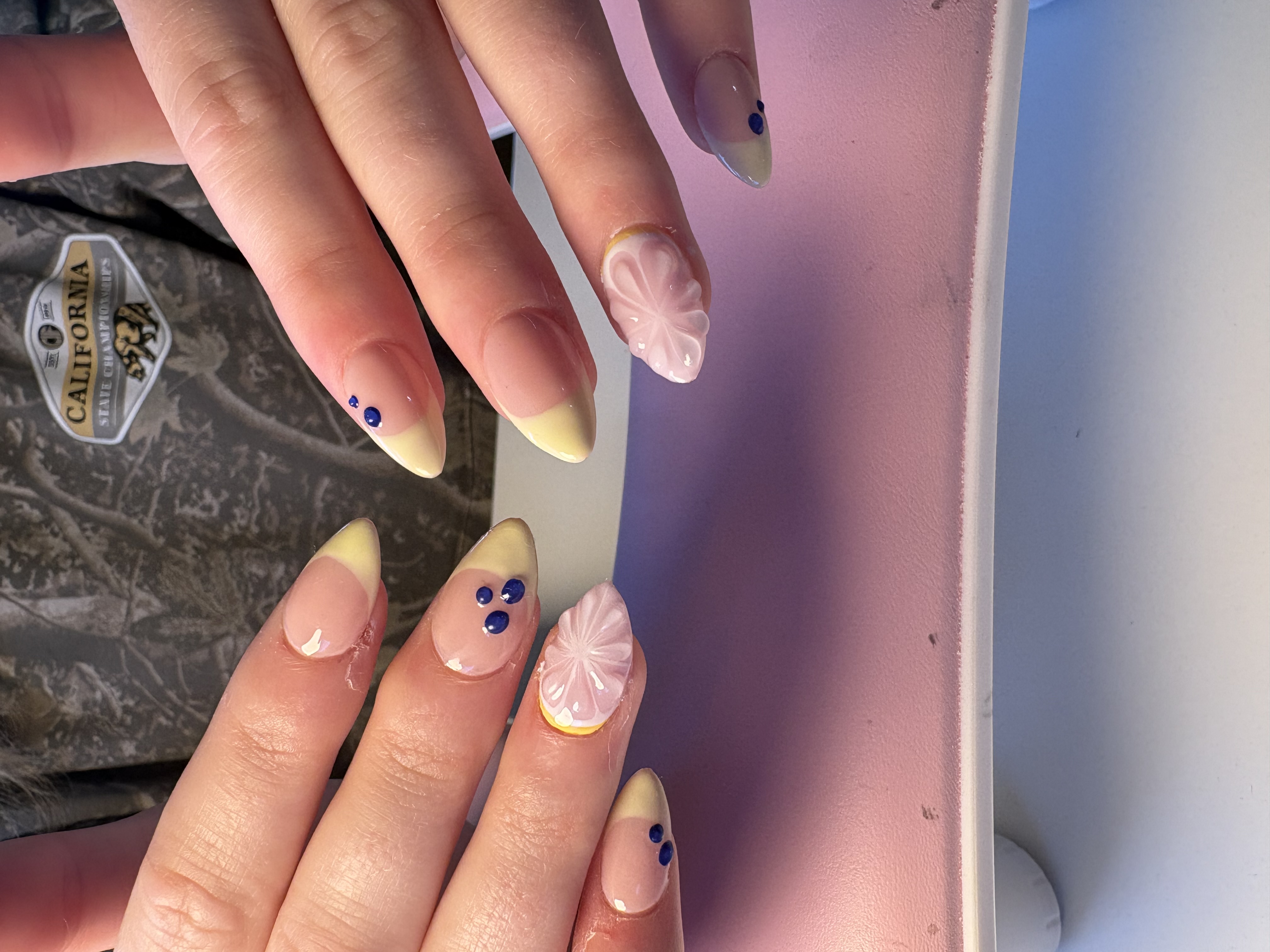 Yellow French tip almond nails with navy dot accents and a 3D sculpted flower