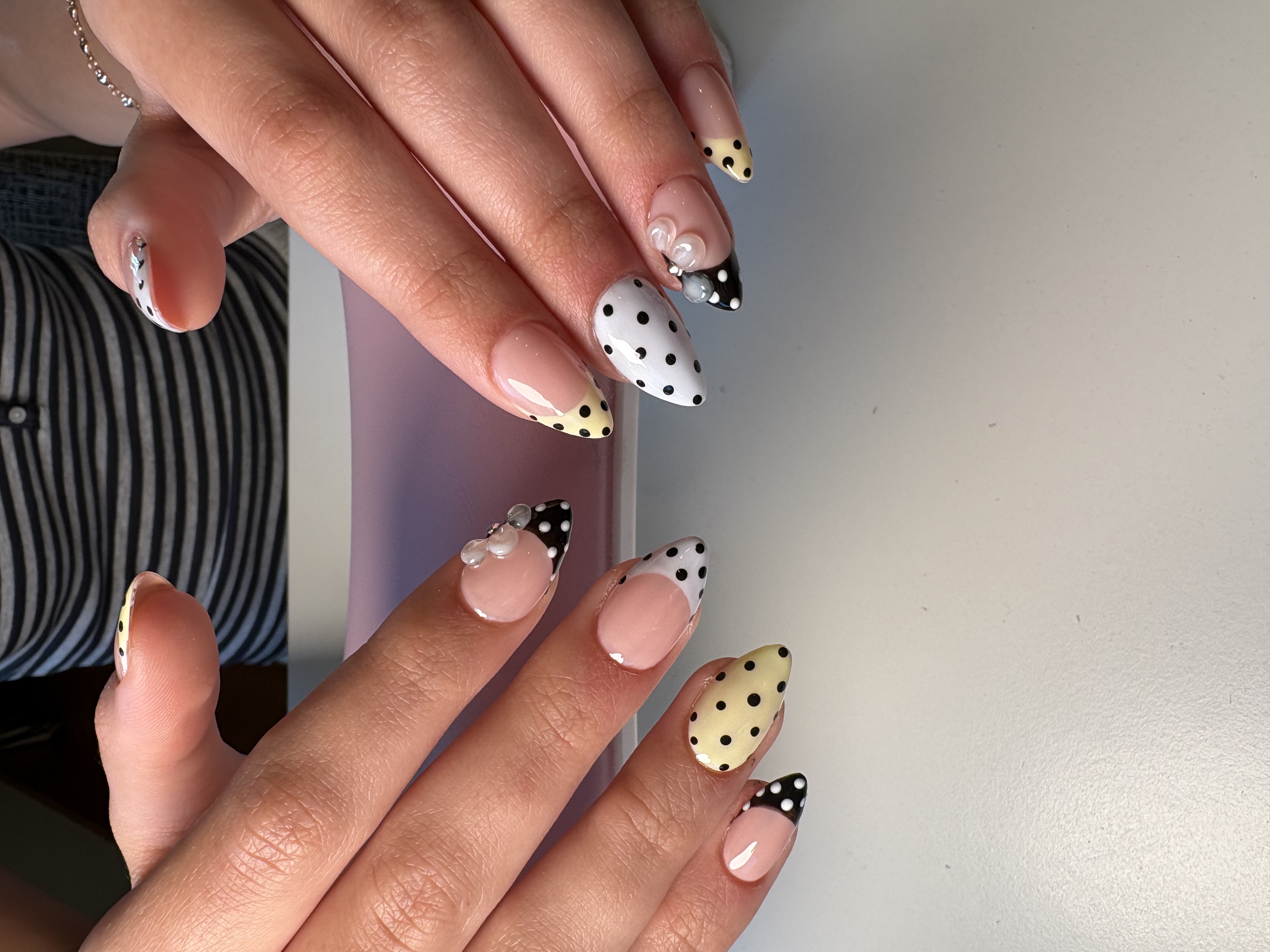 Yellow and white almond nails with black polka dots and a 3D bow accent