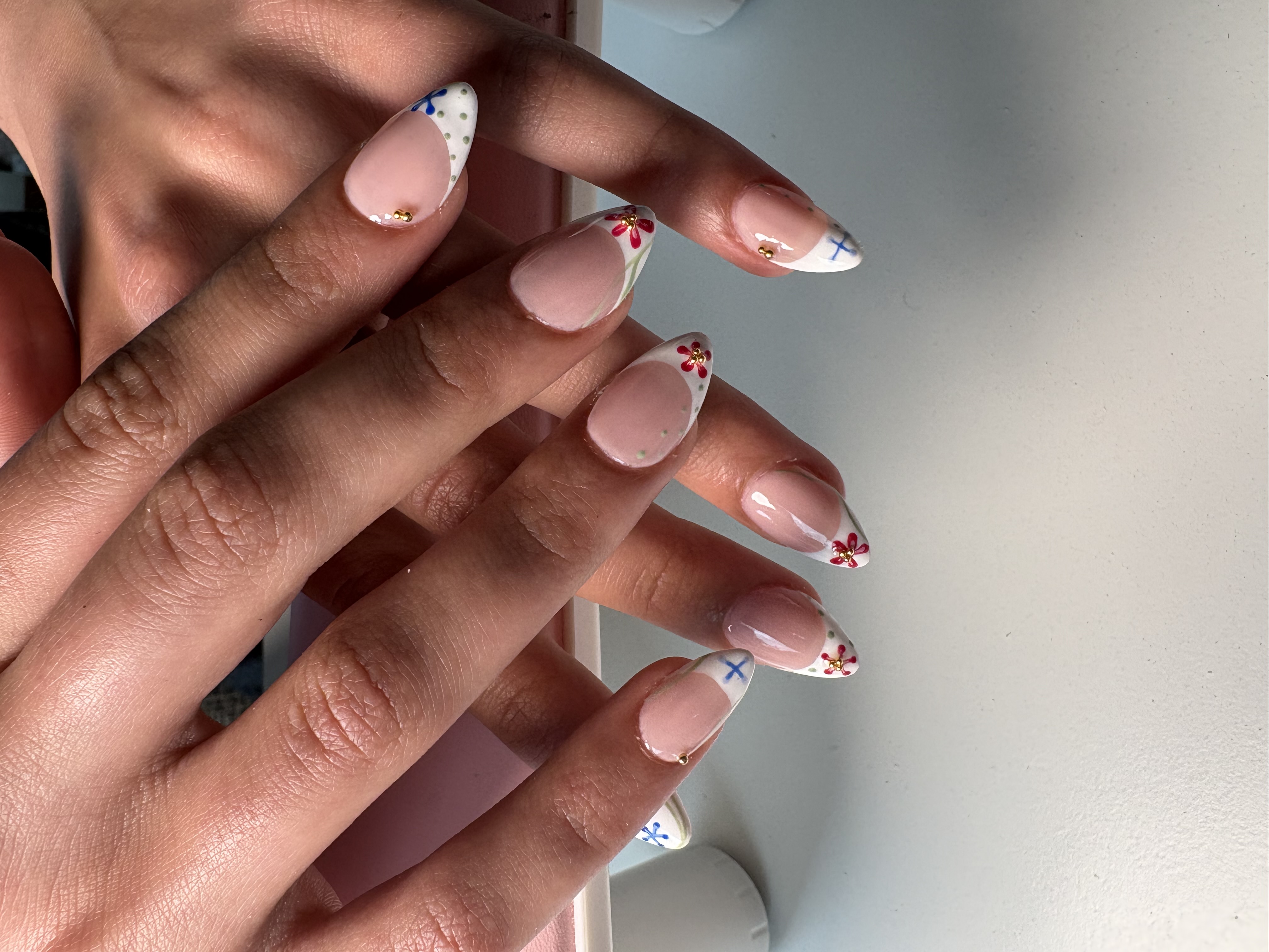 Nude French tip almond nails with tiny hand-painted flowers and gold studs