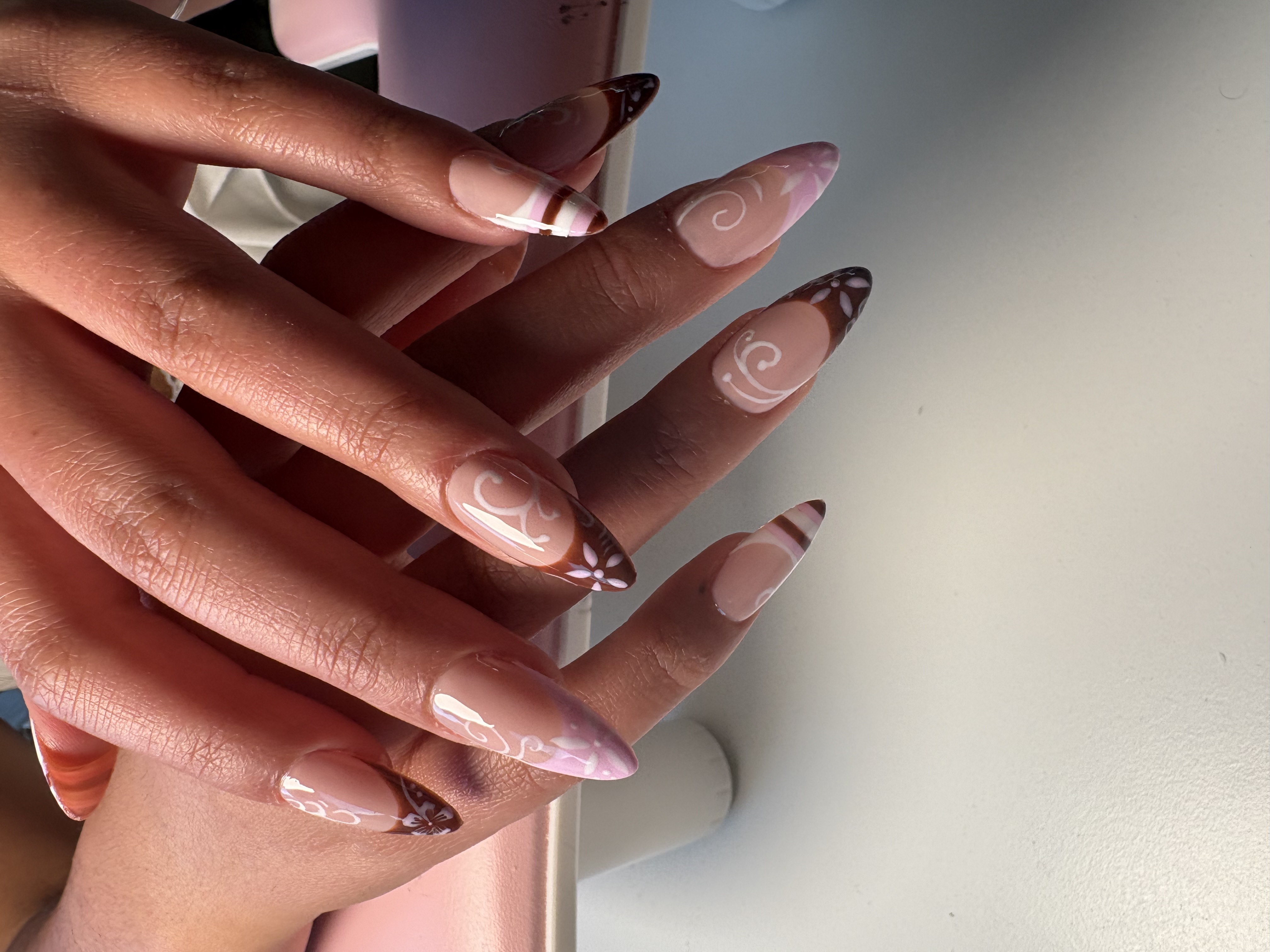 Nude nails with brown French tips and detailed white scroll and floral linework