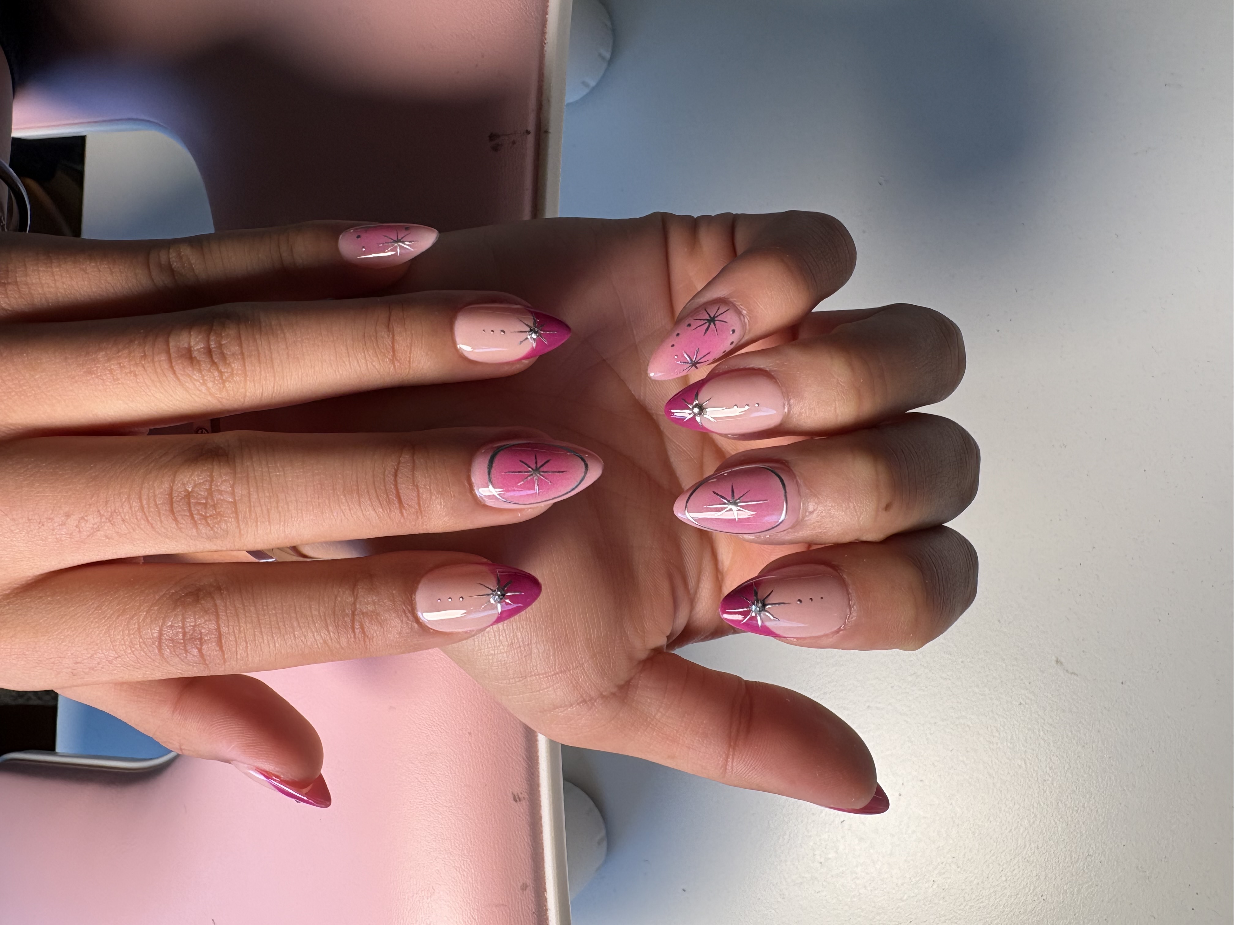 Almond nails with pink ombre base, silver starburst charms, and dotted accents