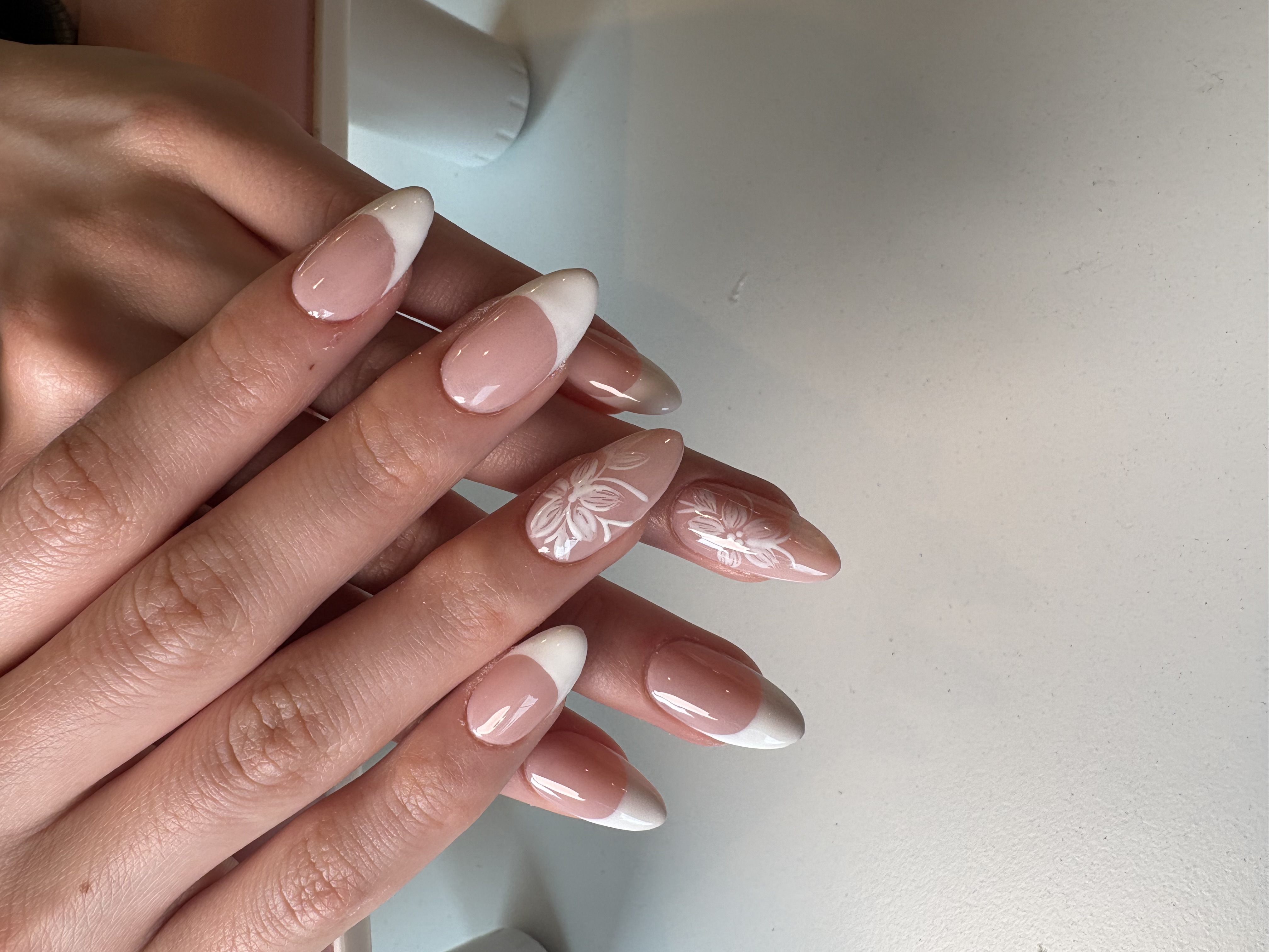 Nude nails with white French tips and two hand-painted white floral accent nails