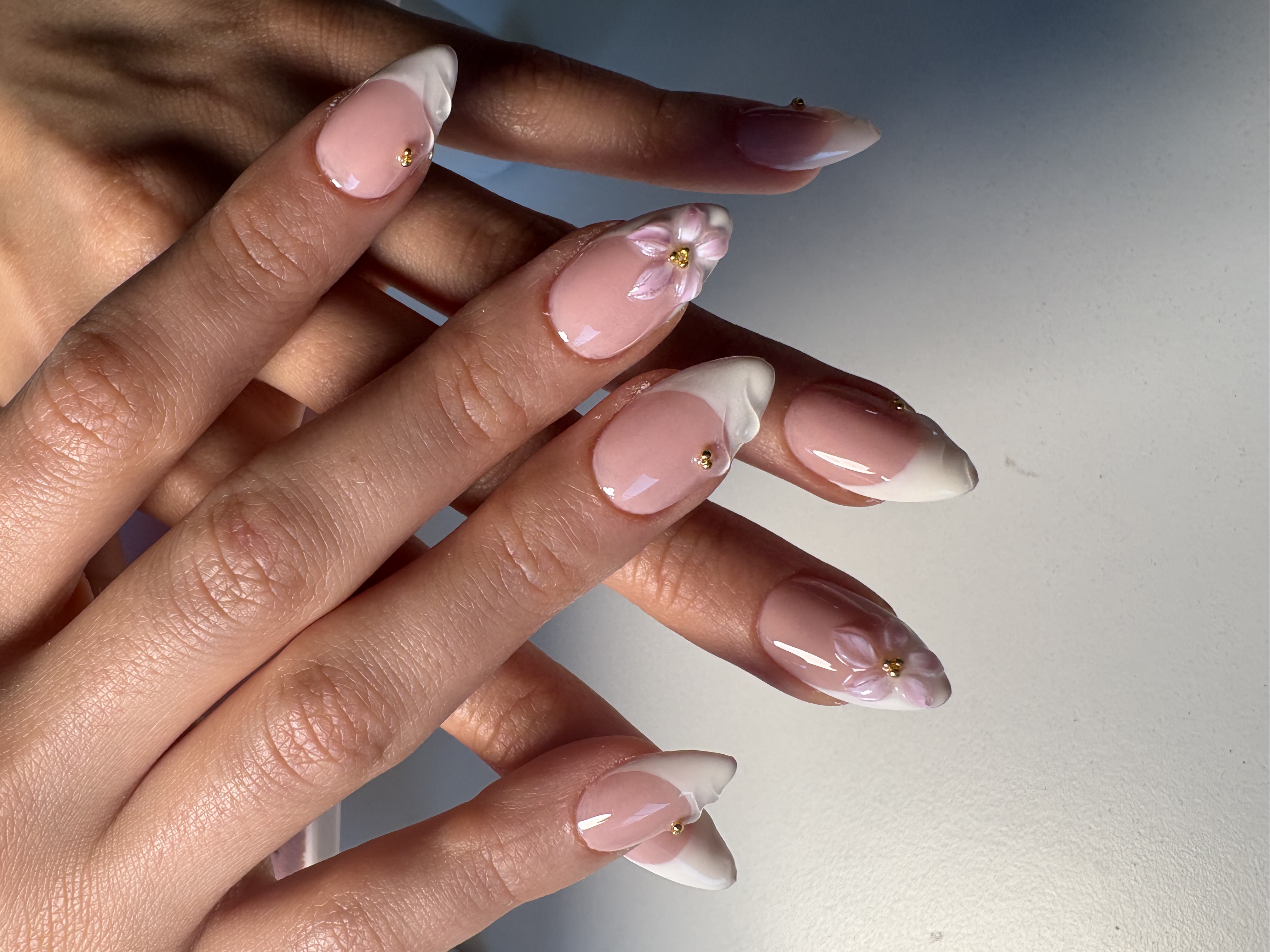 Nude almond nails with white French tips, 3D sculpted flowers, and gold beads