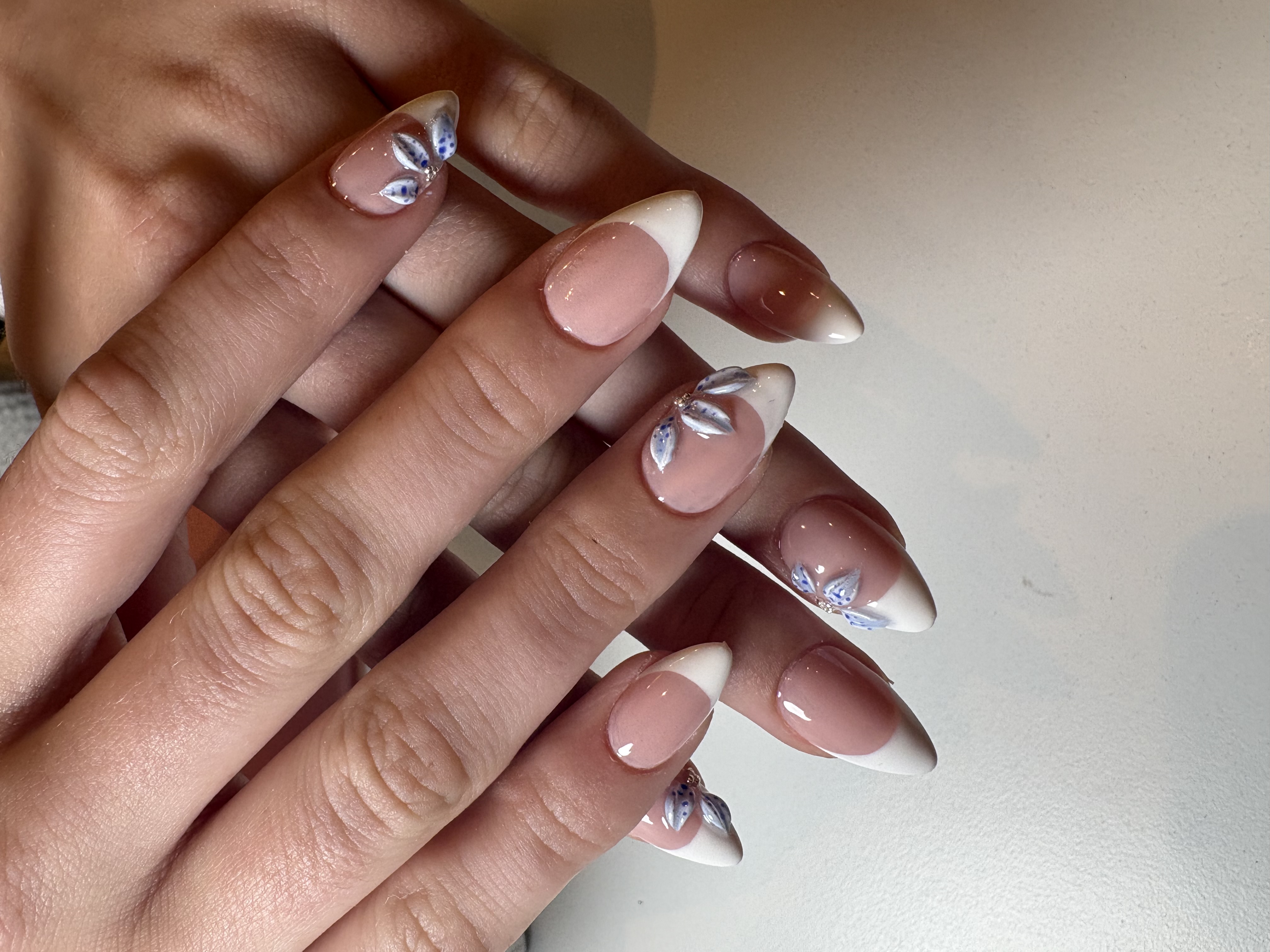 Nude almond nails with white French tips and hand-painted blue floral accent nails