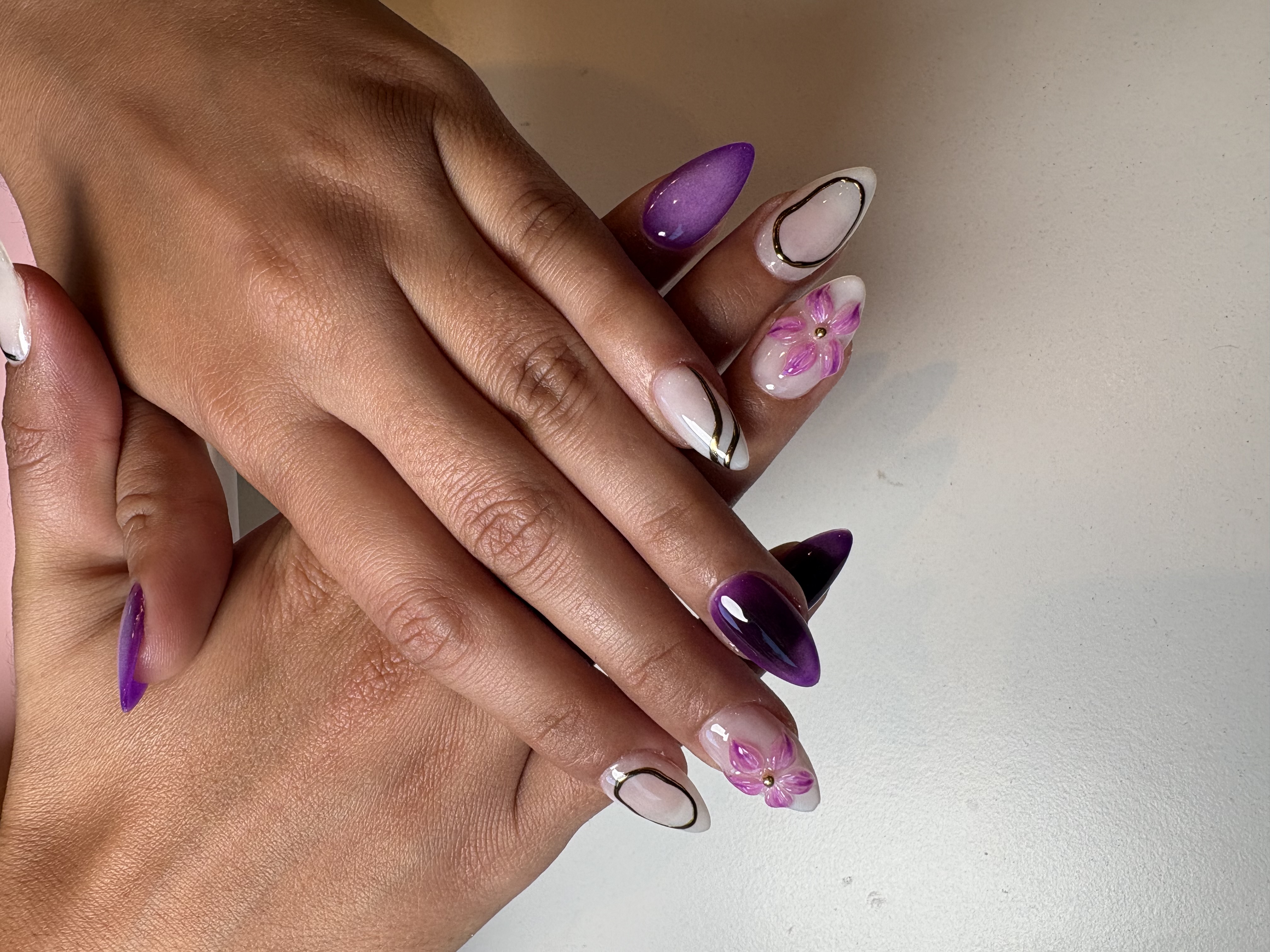 Almond nails mixing solid purple, milky white gold swirl linework, and 3D pink flowers