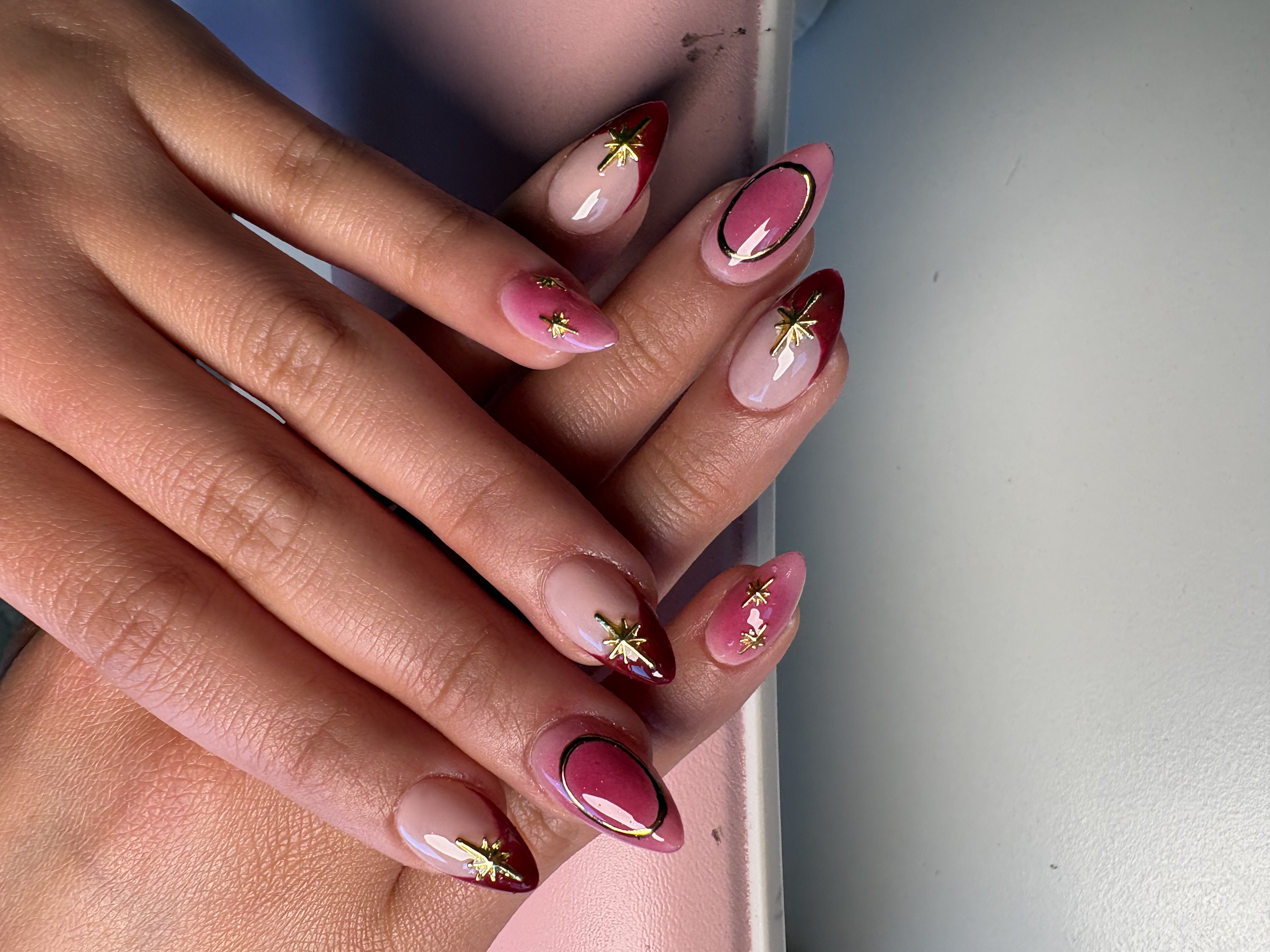 Almond nails with pink ombre base, gold starburst charms, and outlined circle accents