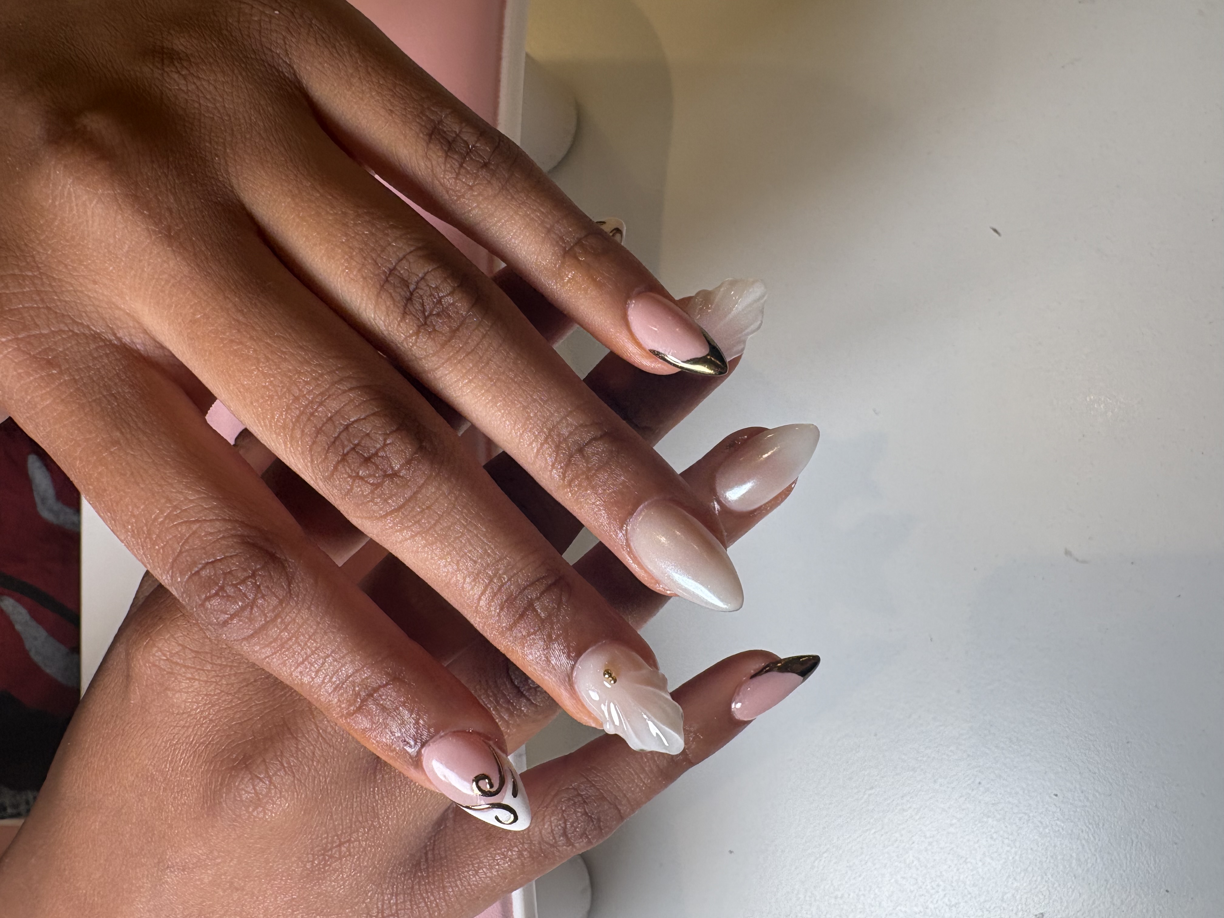 Nude almond nails with a 3D sculpted white flower and gold swirl linework accent