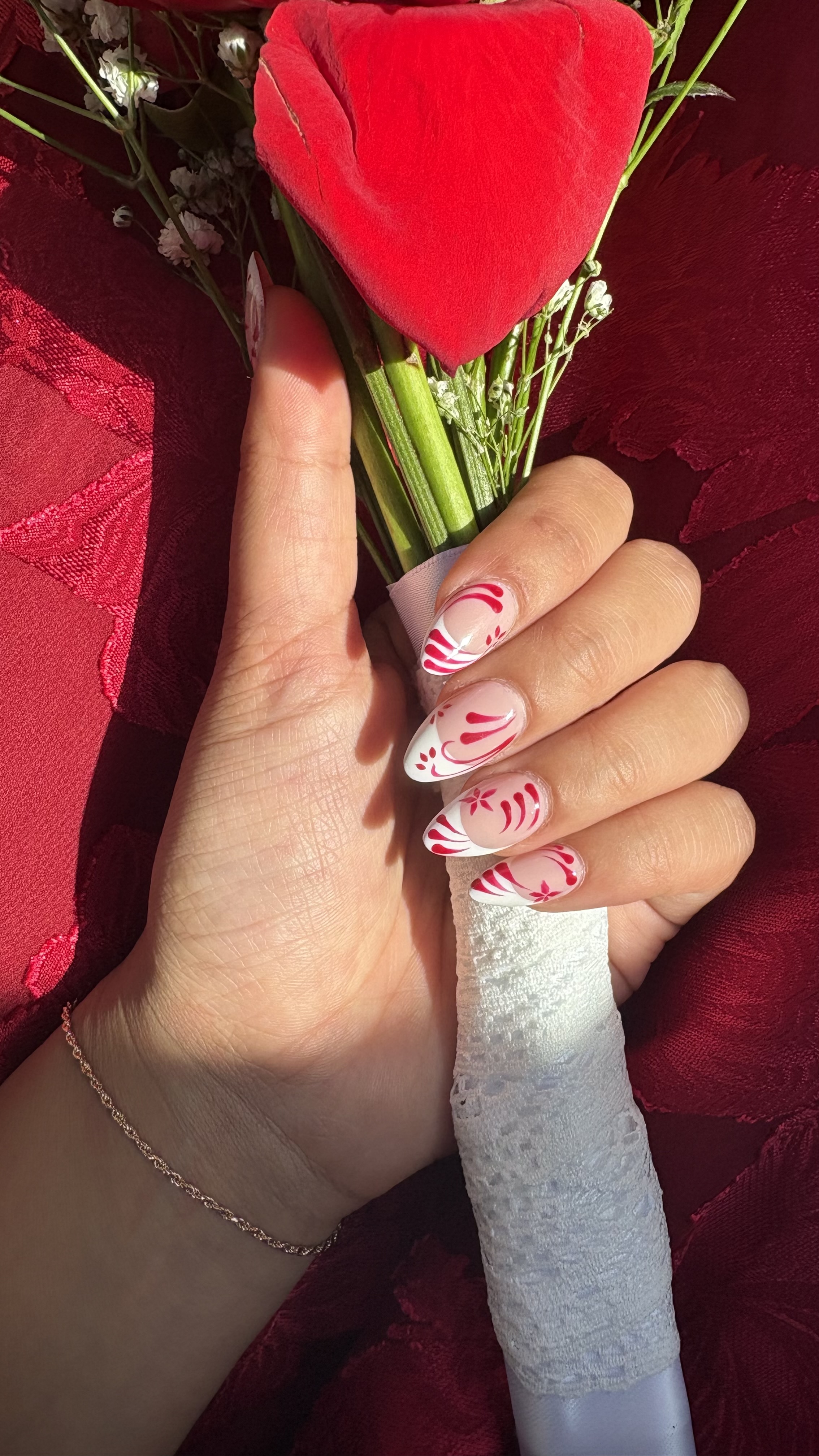 Square nails with red French tips and hand-painted red floral flourish details