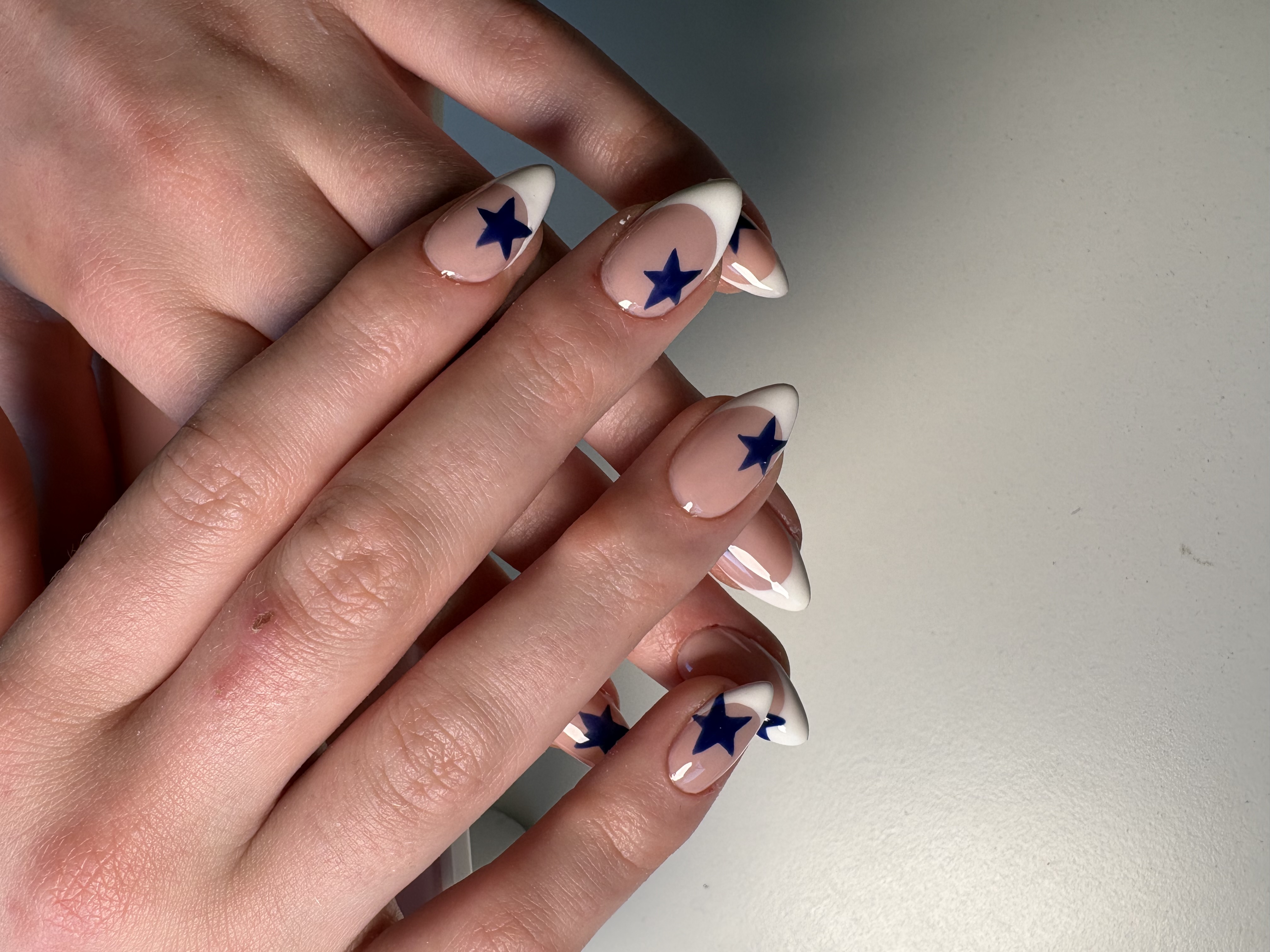 Almond nails with white French tips and hand-painted navy stars and crescent moons