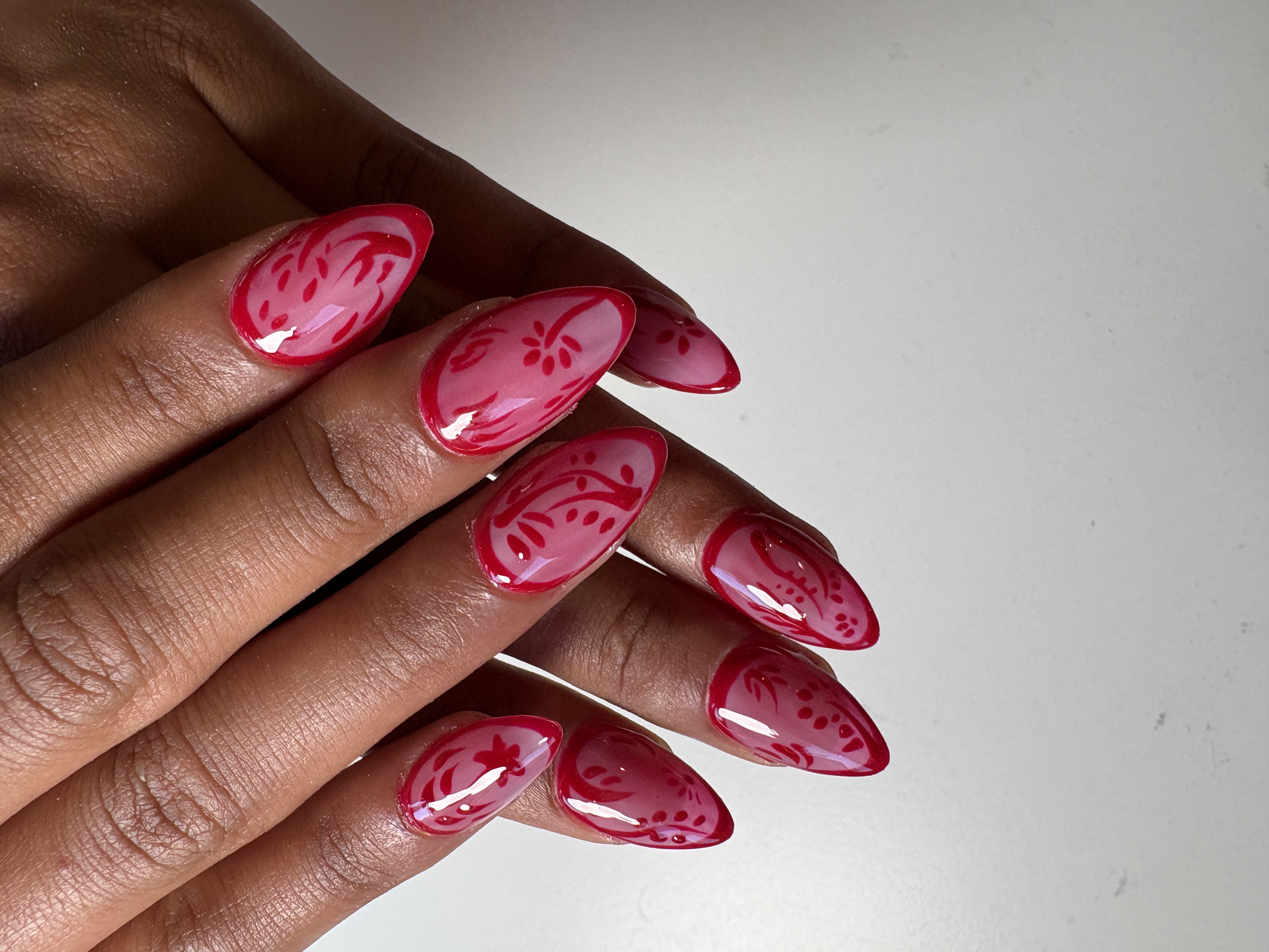 Almond nails with pink gradient base and detailed maroon floral scroll linework throughout