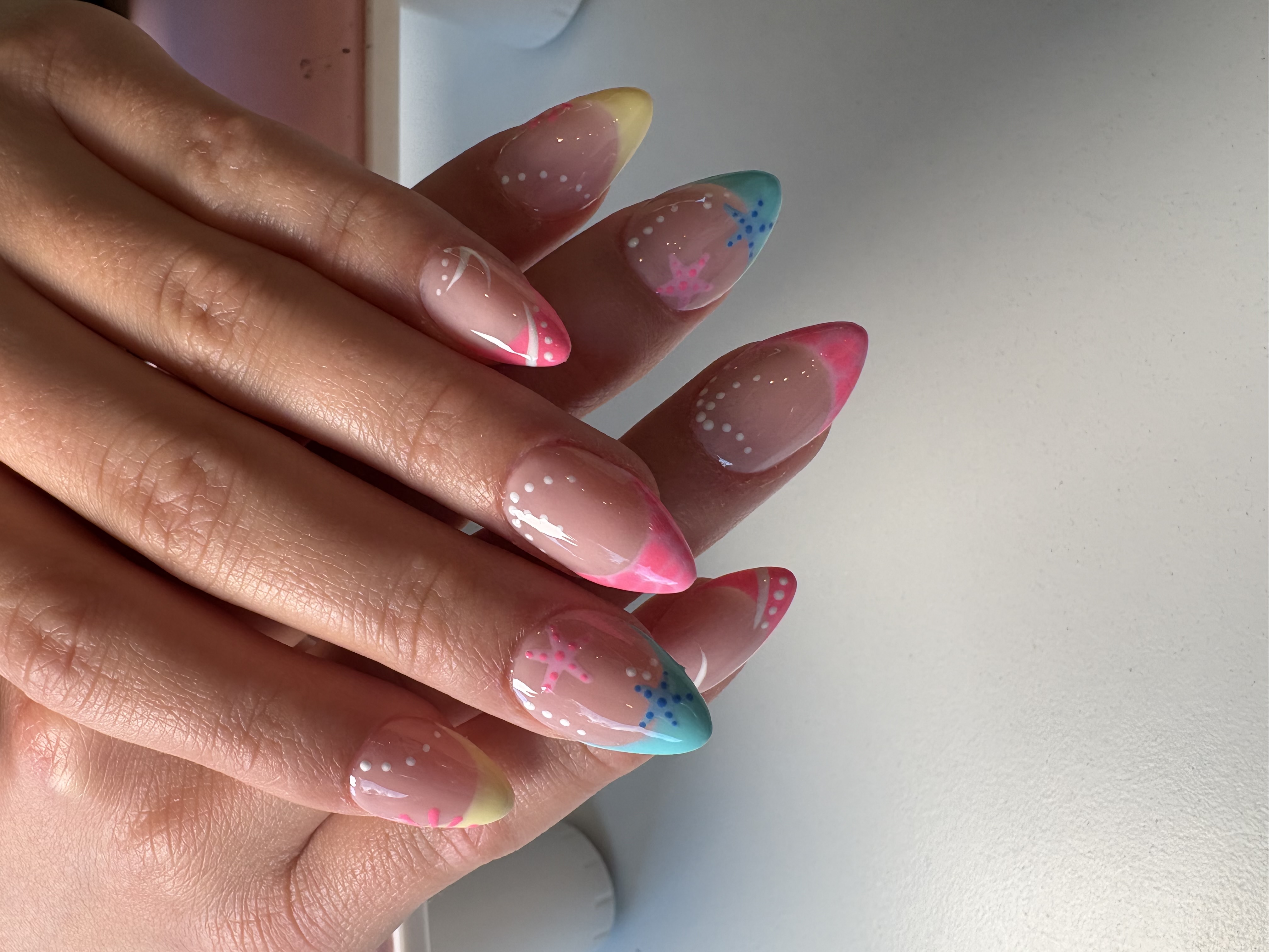 Nude almond nails with pastel French tips, white dots, and painted starfish accents