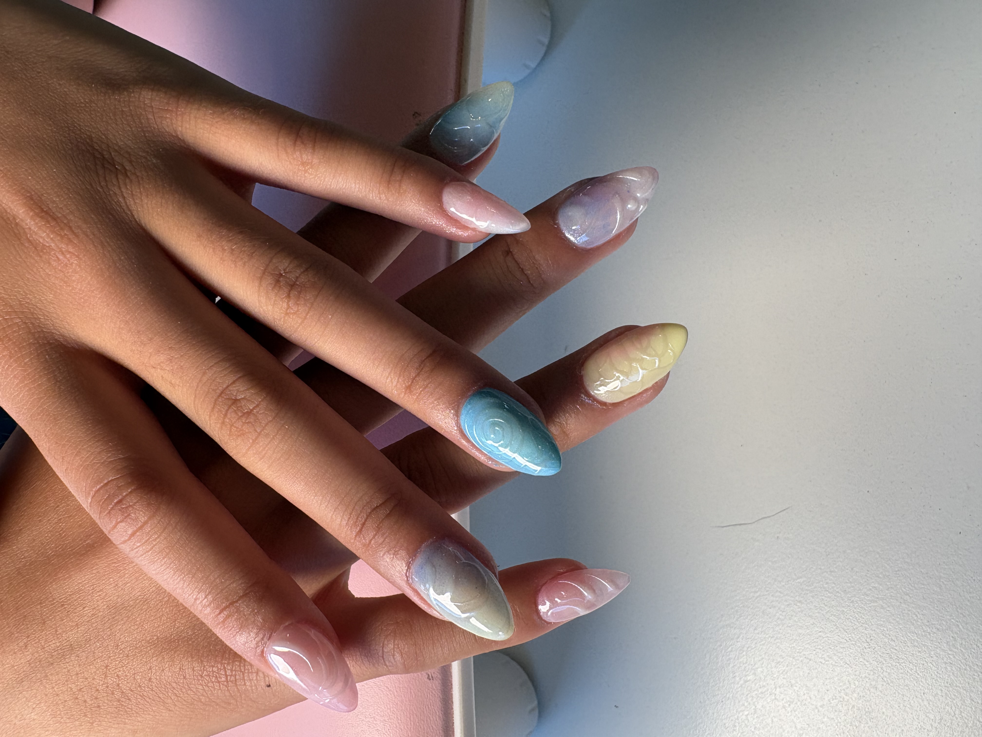 Pastel almond nails in blue, lilac, and yellow with subtle marbled swirl texture