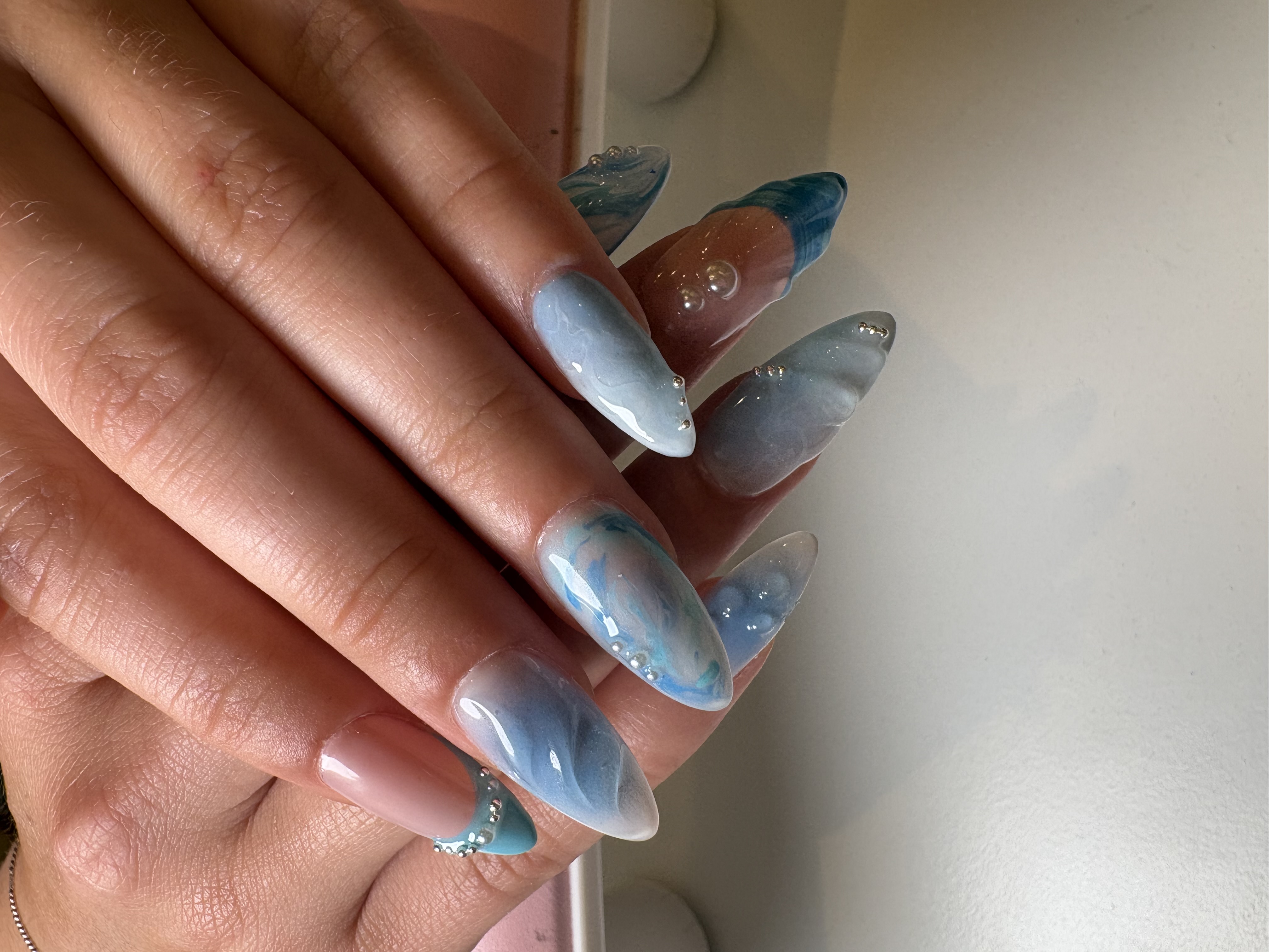 Blue-gray stiletto nails with marbled chrome swirls, silver studs, and 3D bubble accents
