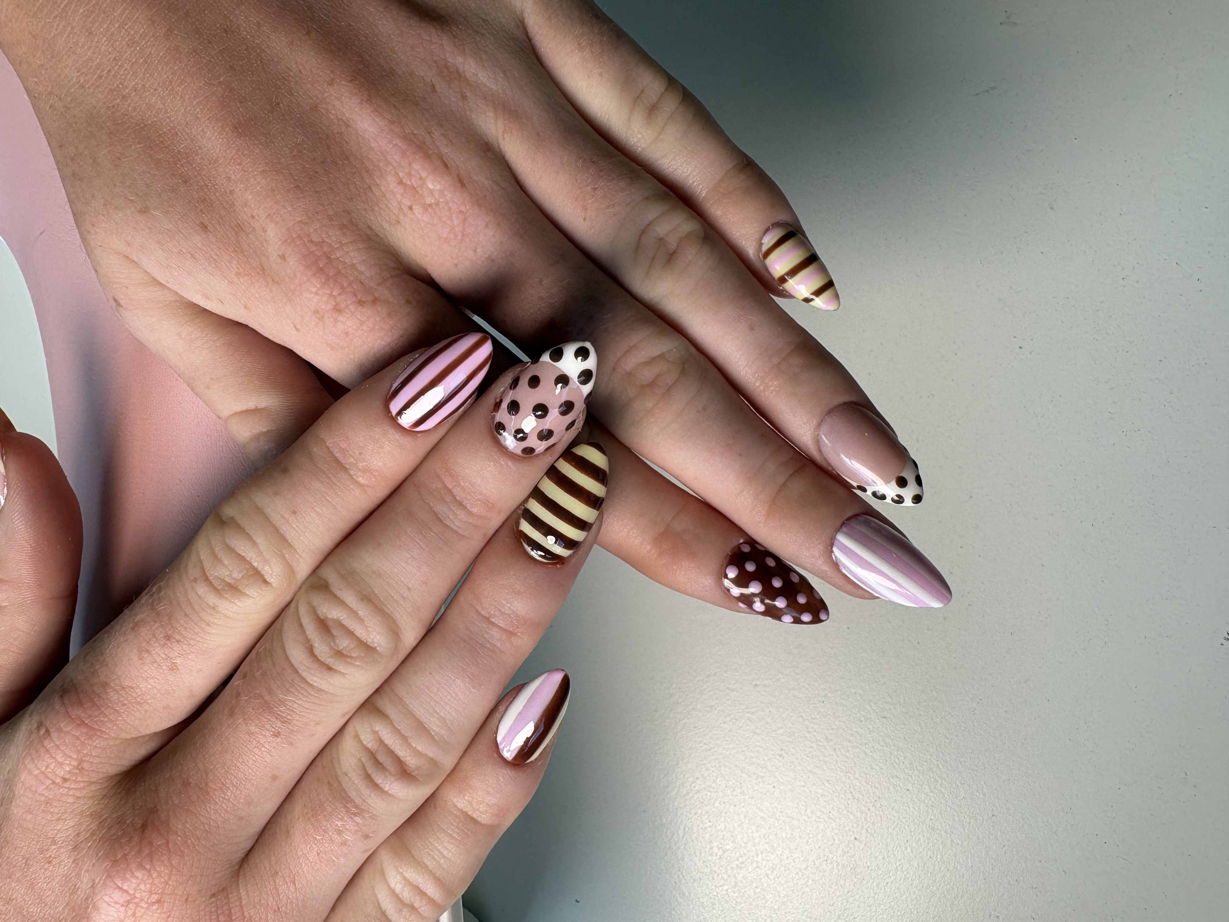 Nude almond nails with brown-and-pink candy stripes and chocolate polka dot accents