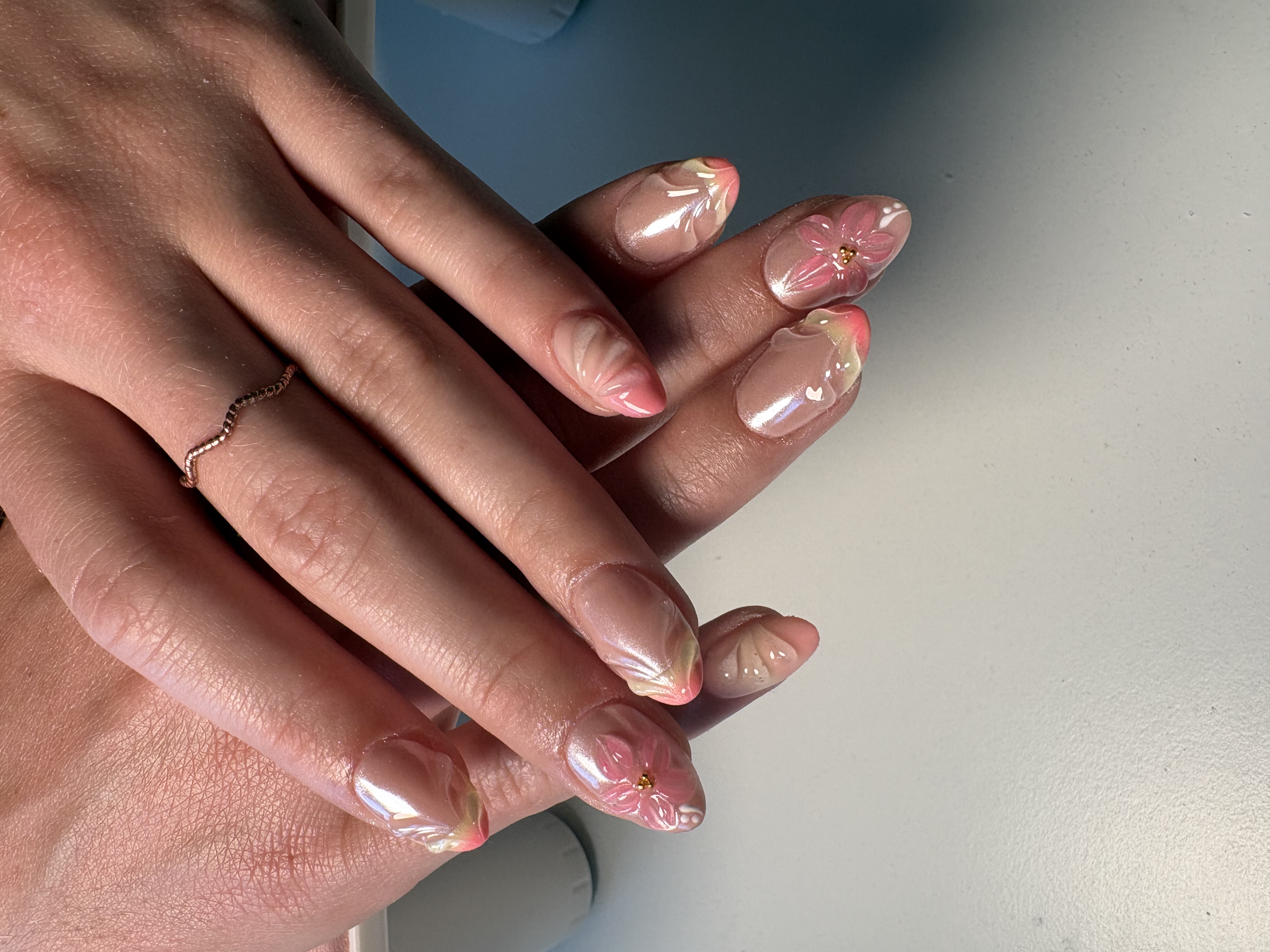 Sheer nude almond nails with pink ombre tips and hand-painted flowers with gold centers