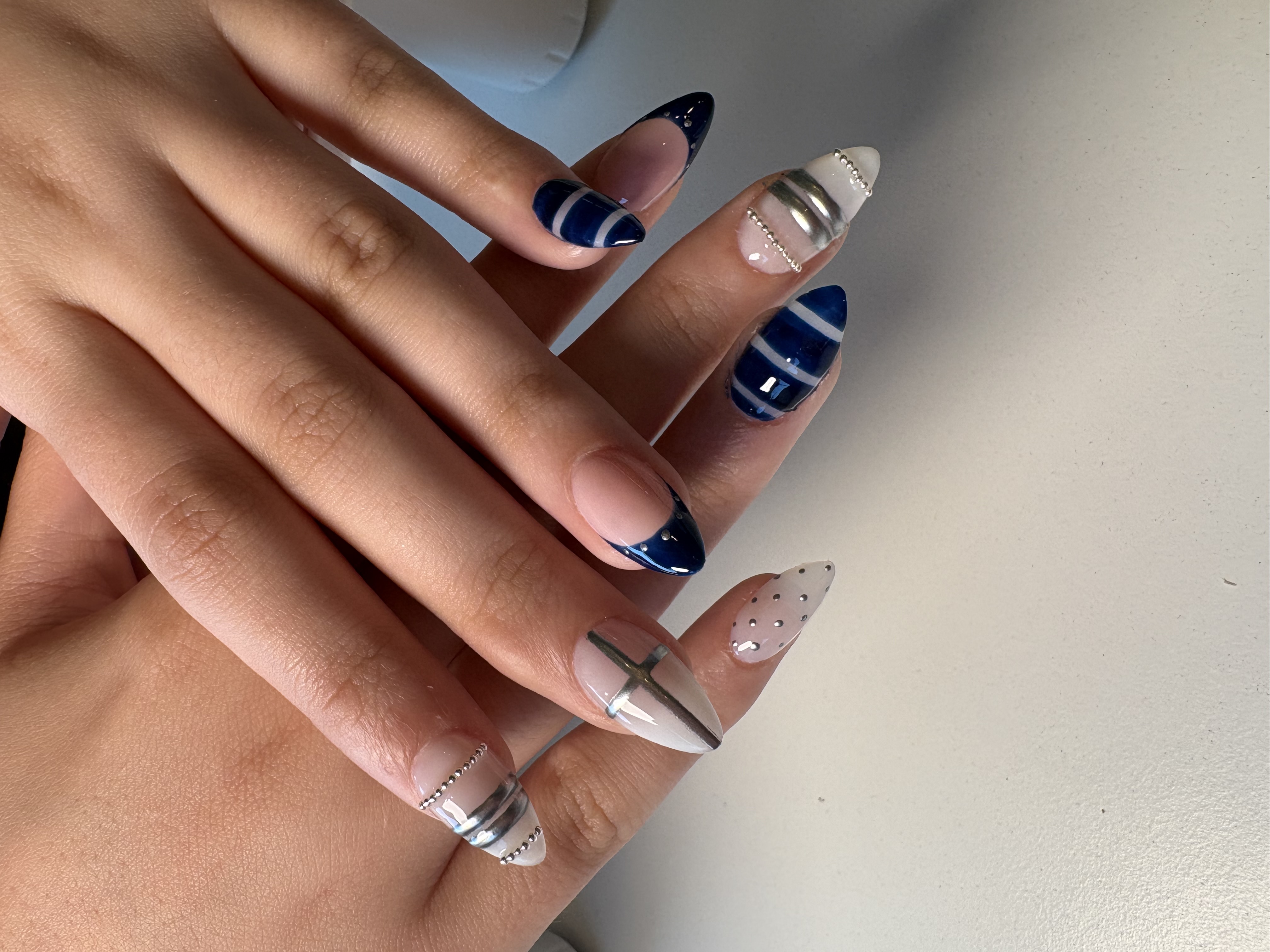 Navy and white stiletto nails with silver chrome linework, negative space, and rhinestone accents