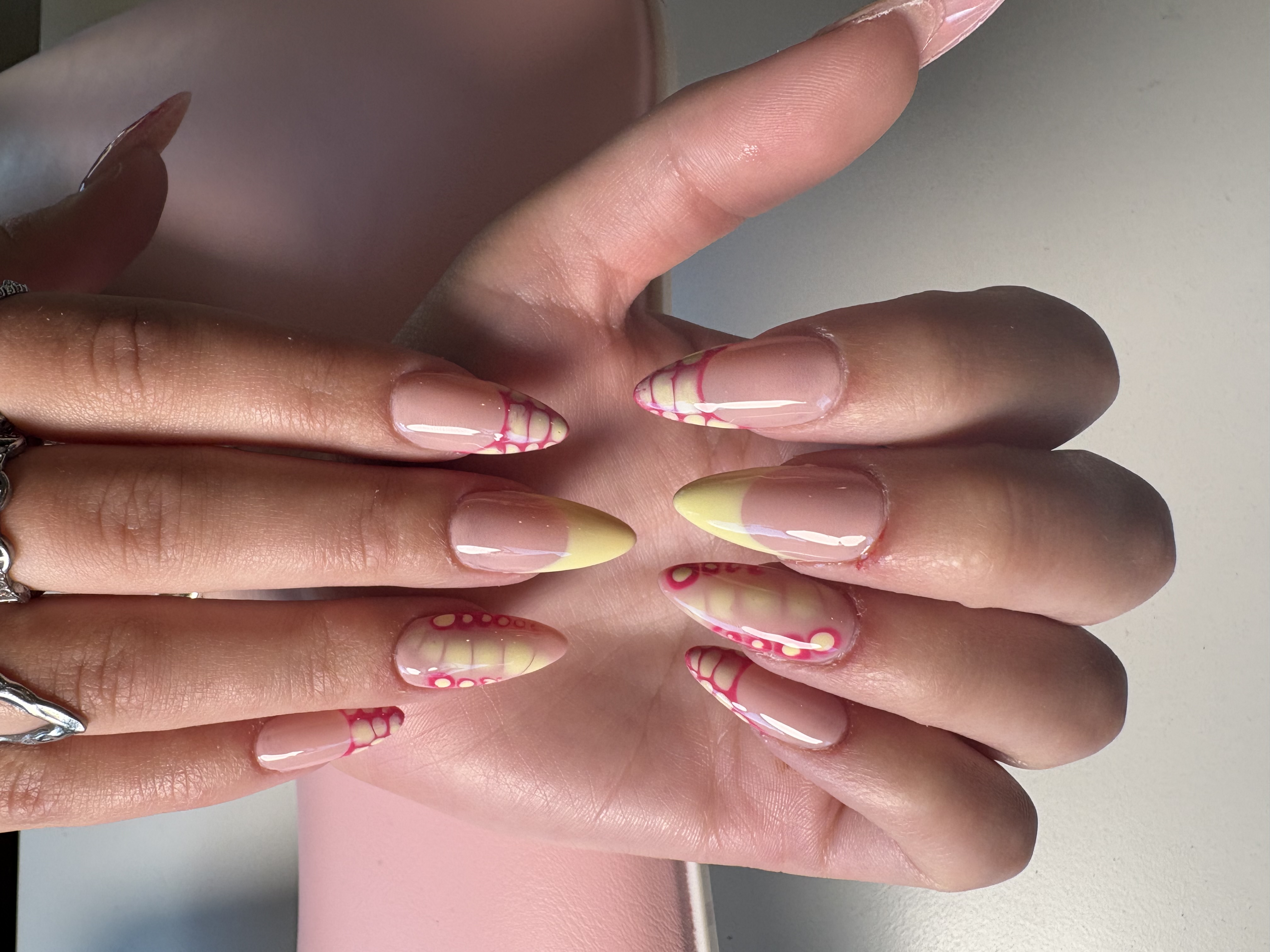 Nude almond nails with pink and yellow lace-web patterned French tips