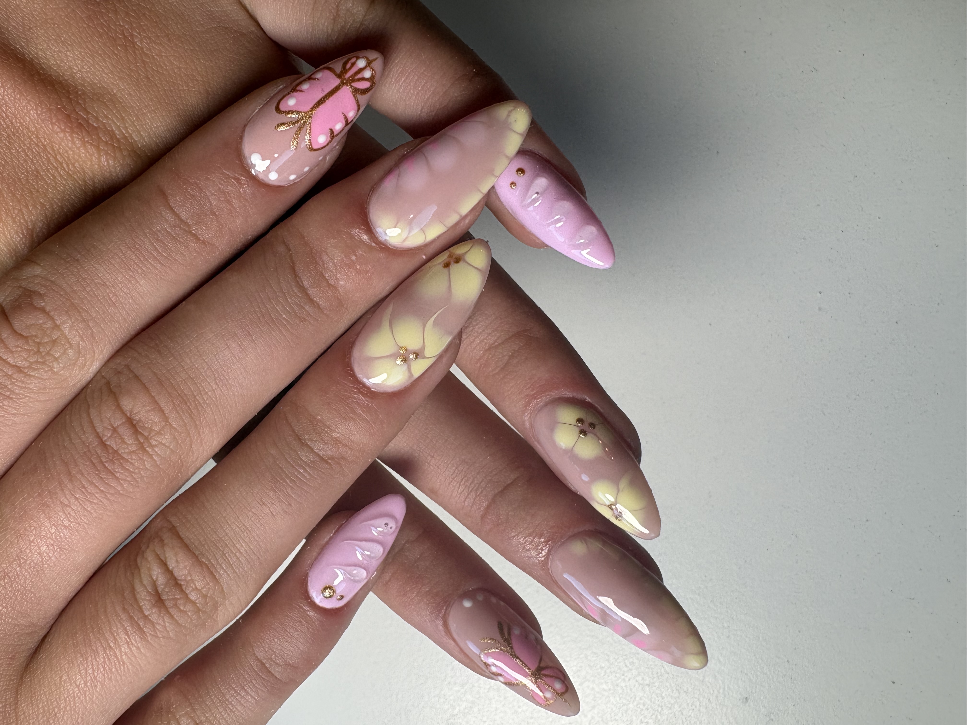Nude almond nails with a gold-outlined pink butterfly and dimensional floral accents