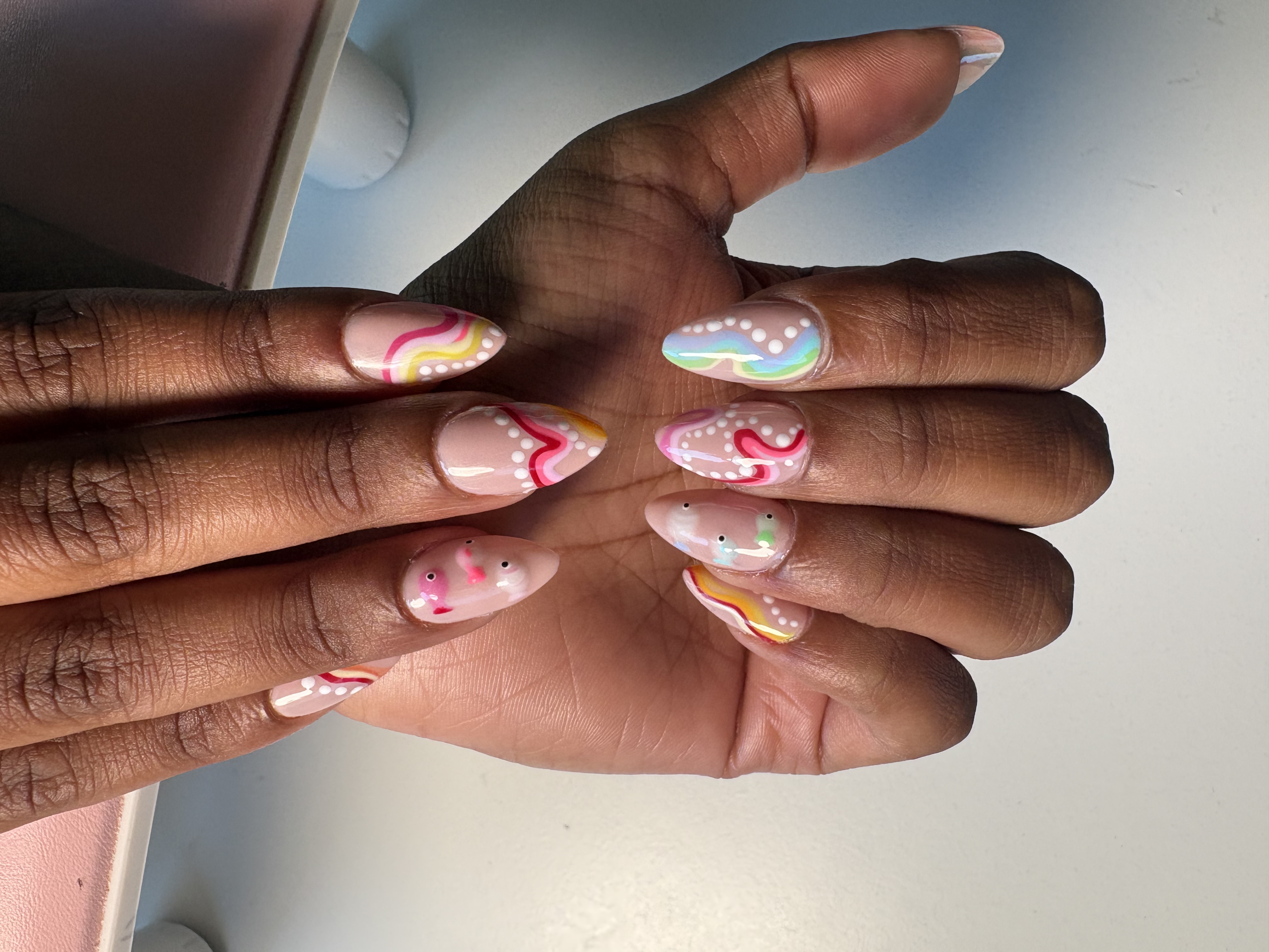 Nude almond nails with pastel rainbow squiggle linework and scattered white dot accents