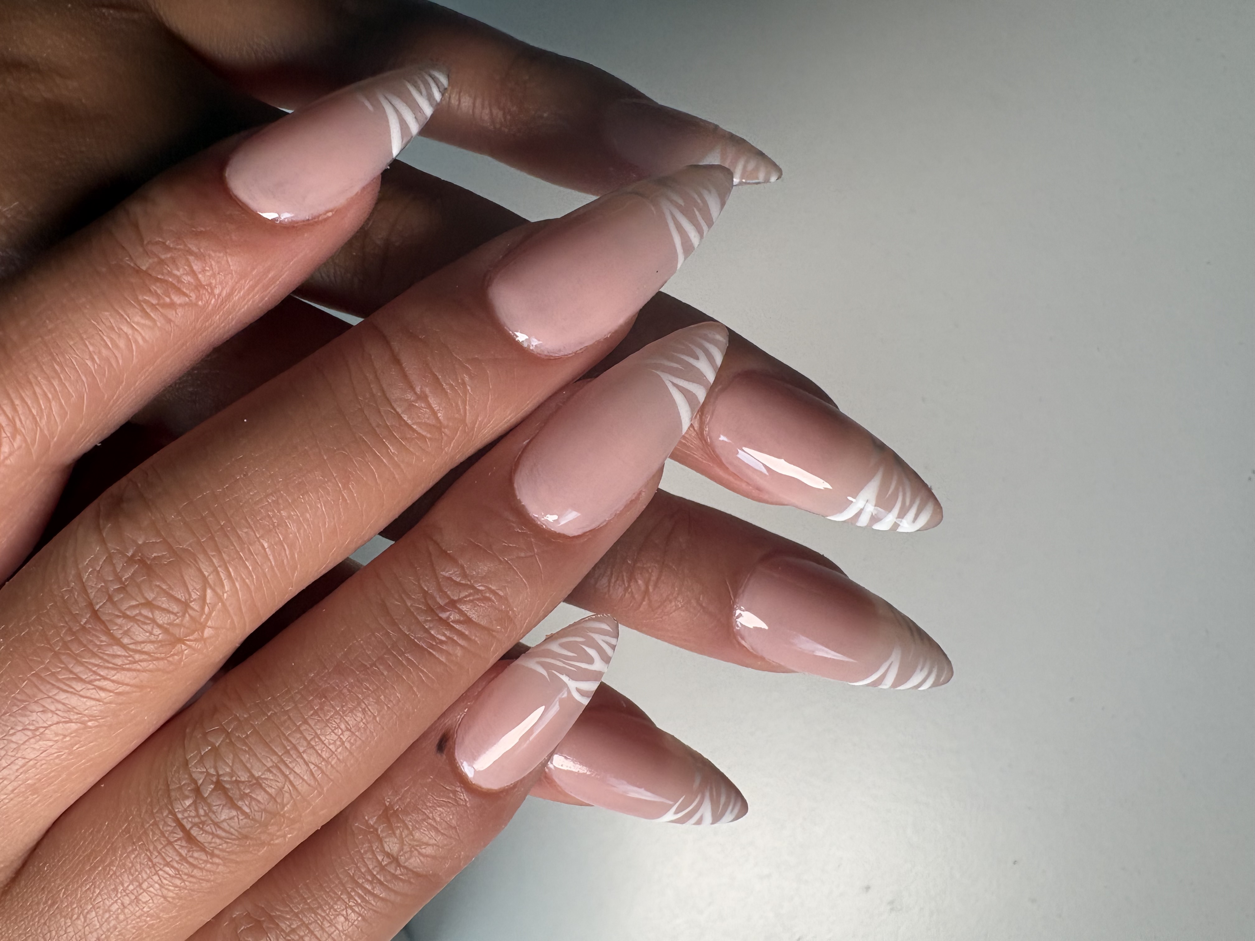 Nude almond nails with fine white zebra-stripe linework over a sheer clear base