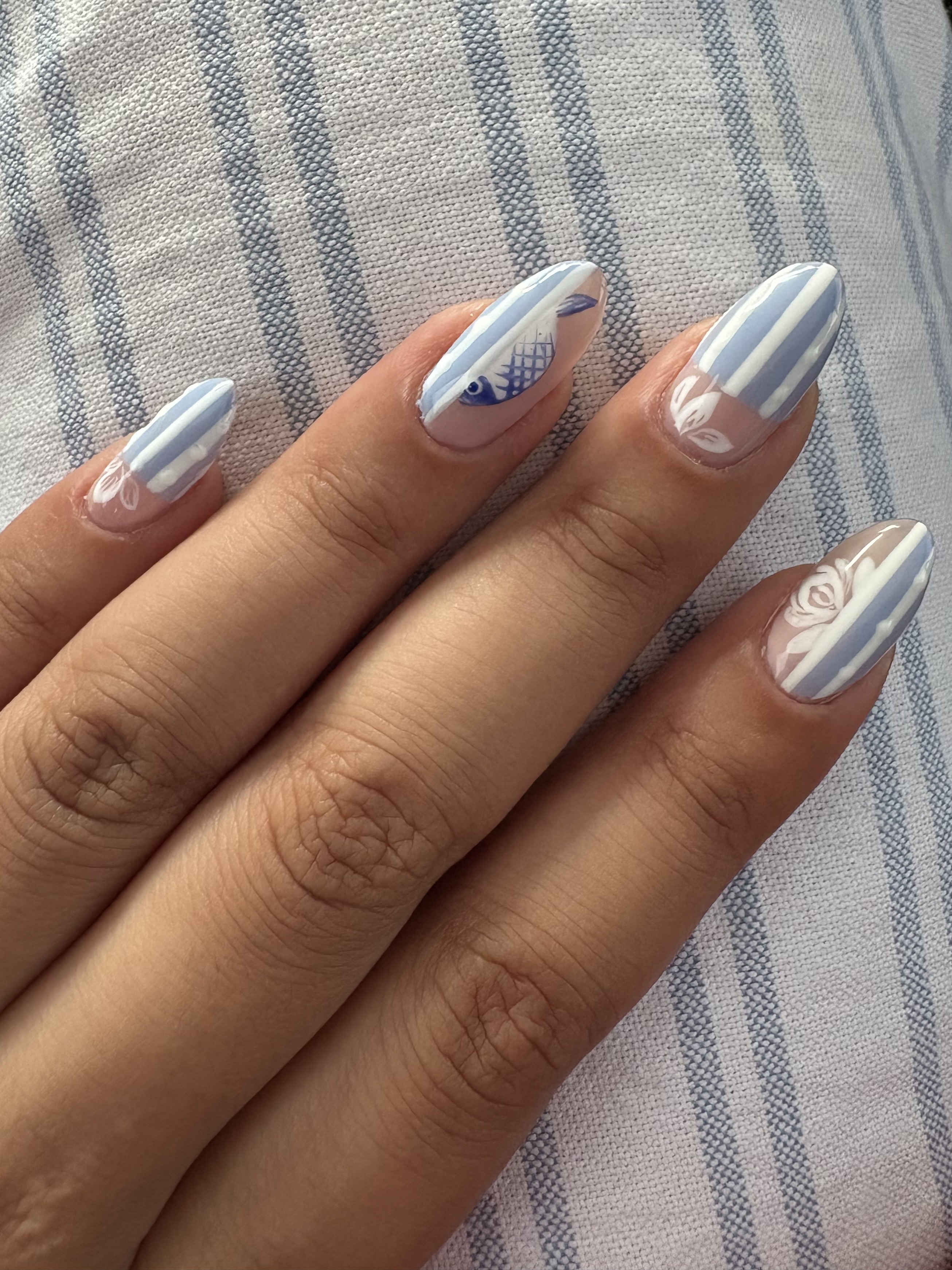 Blue-and-white striped almond nails with a hand-painted fish and rose accent design