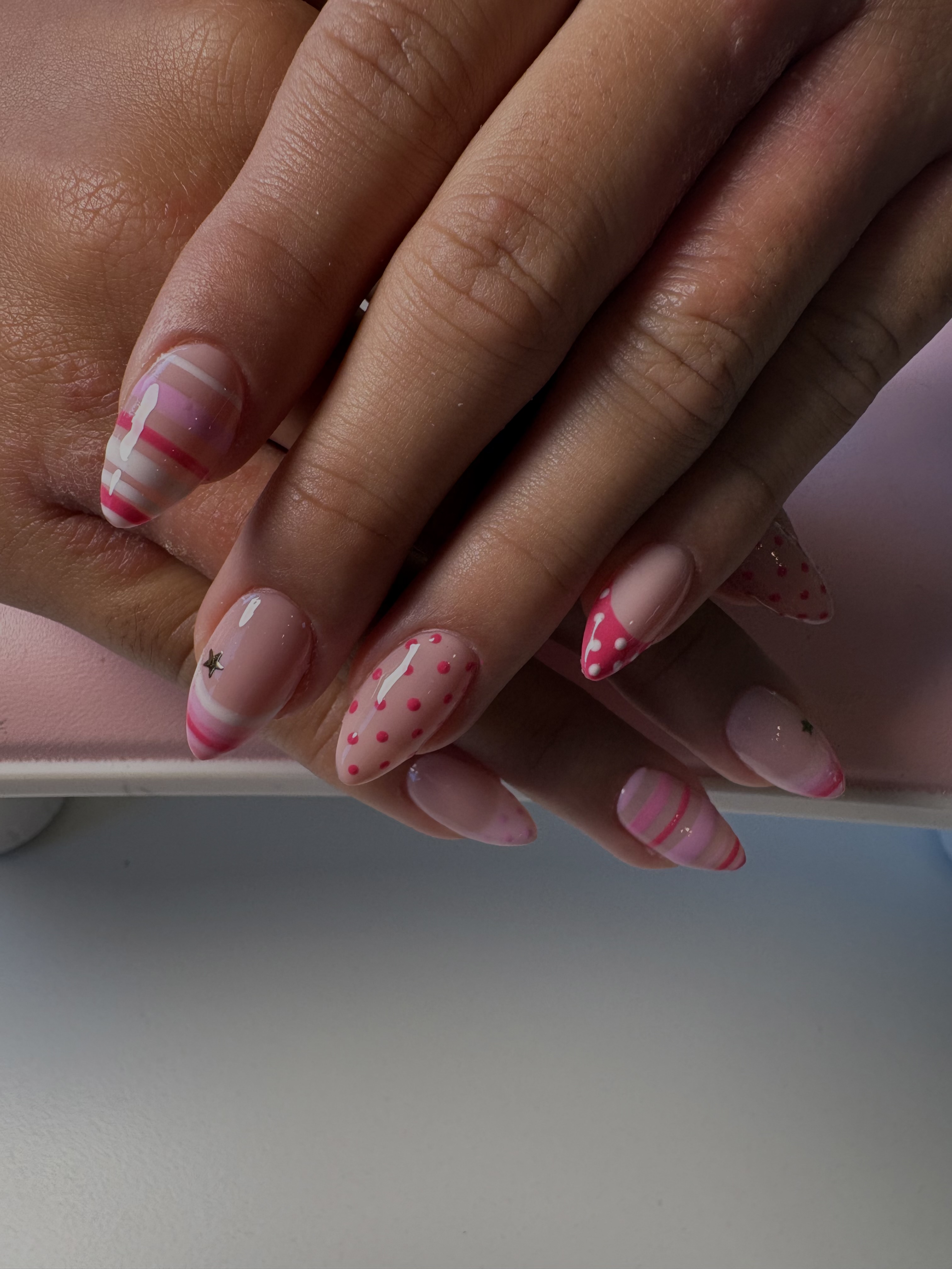 Nude and pink almond nails with polka dots, thin stripes, and a gold star